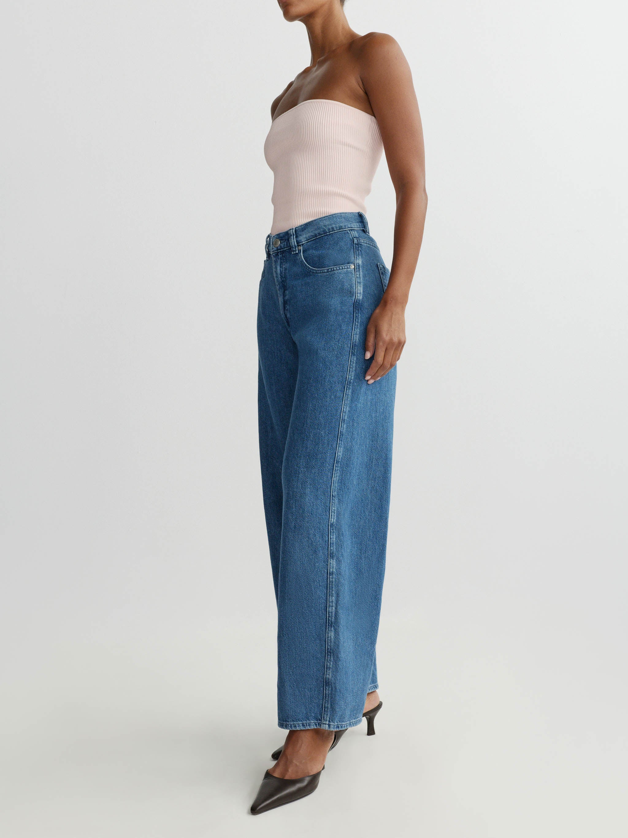 Woman wearing a strapless top and wide-leg jeans on a plain background