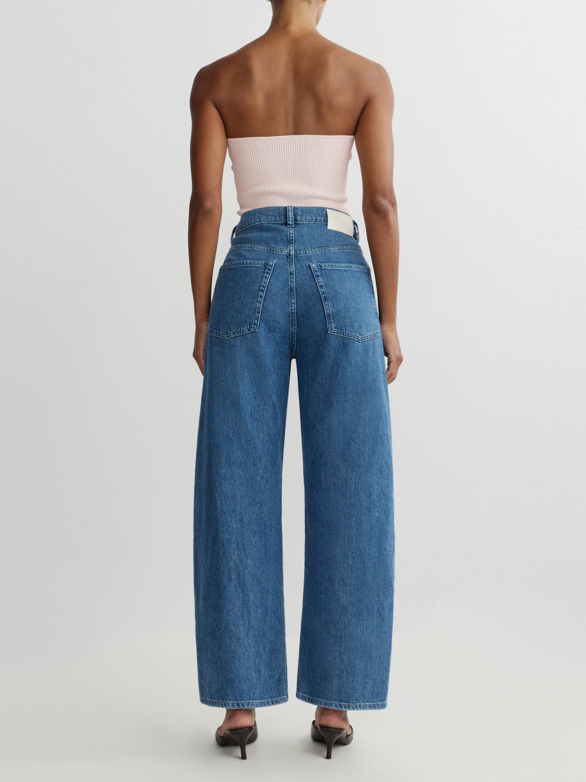 Person wearing strapless top and blue jeans on a white background