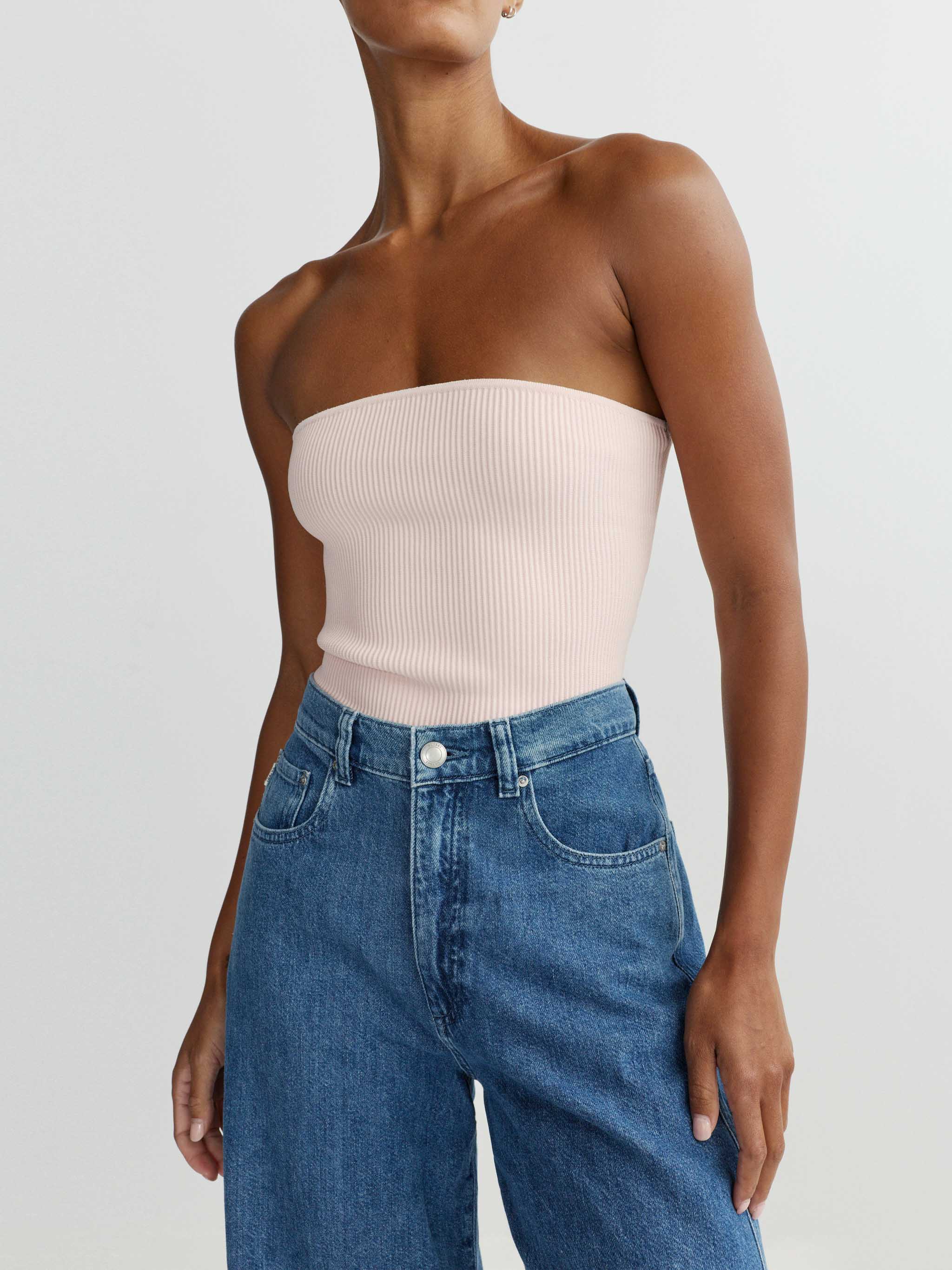 Person wearing a strapless top and blue jeans on a plain background