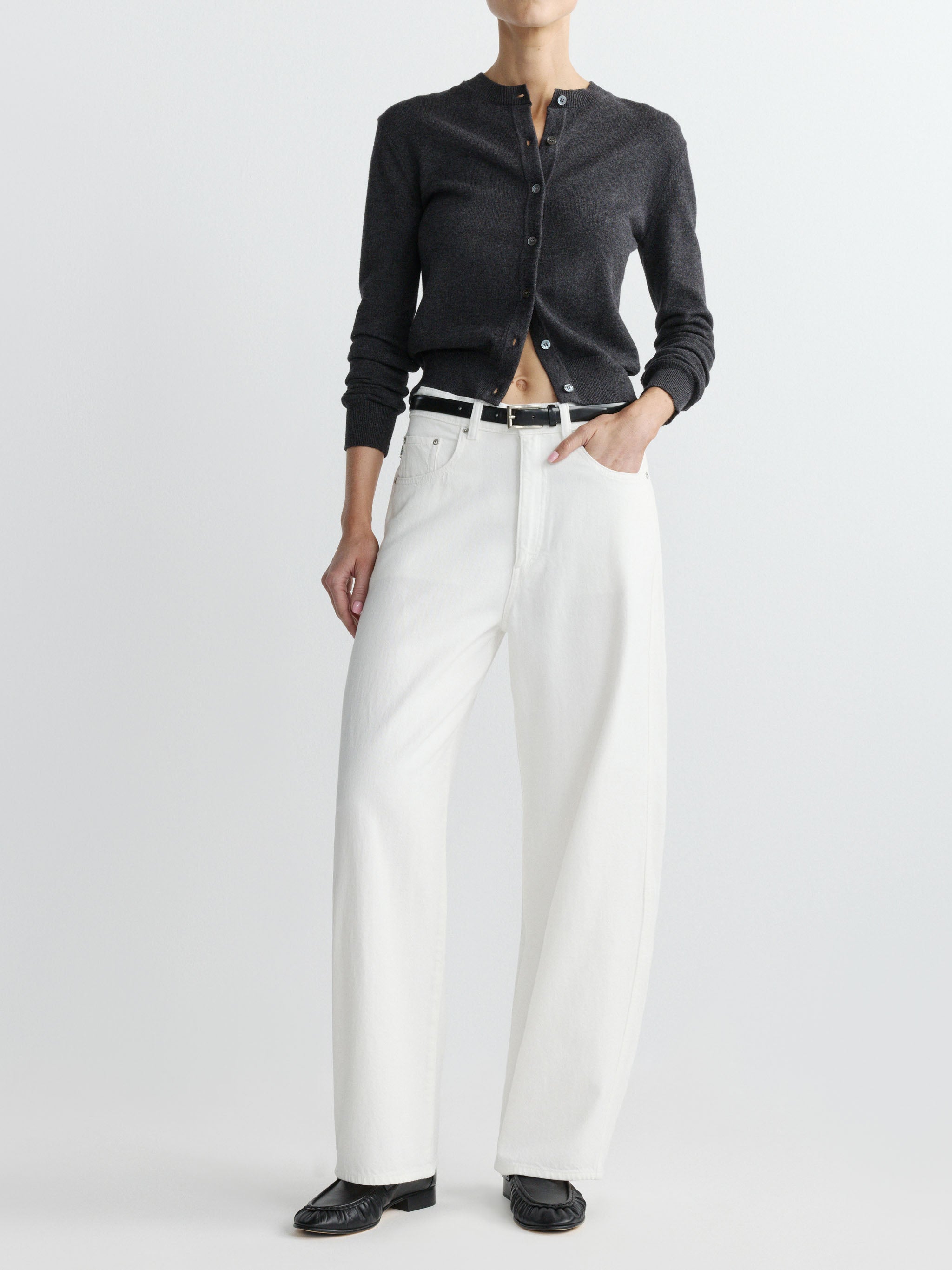 Person wearing a dark grey cardigan, white pants, and black shoes on a white background