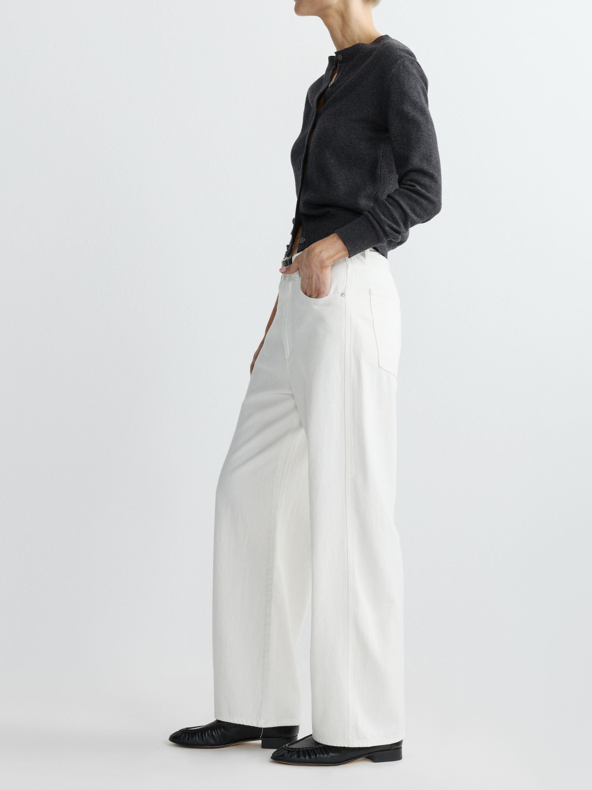 Person wearing a dark grey sweater and white pants on a plain background