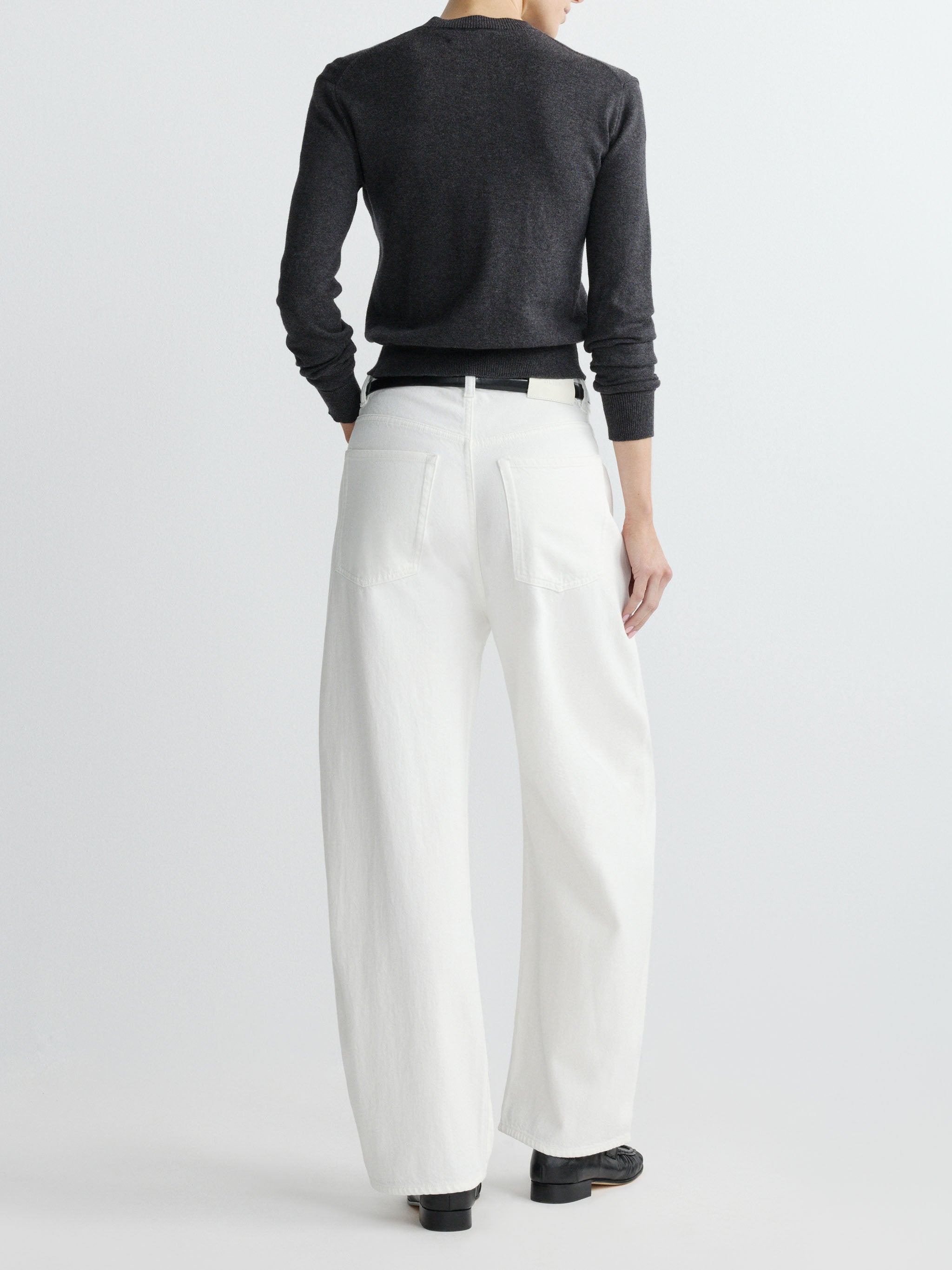 Person wearing a dark sweater and white pants on a plain background