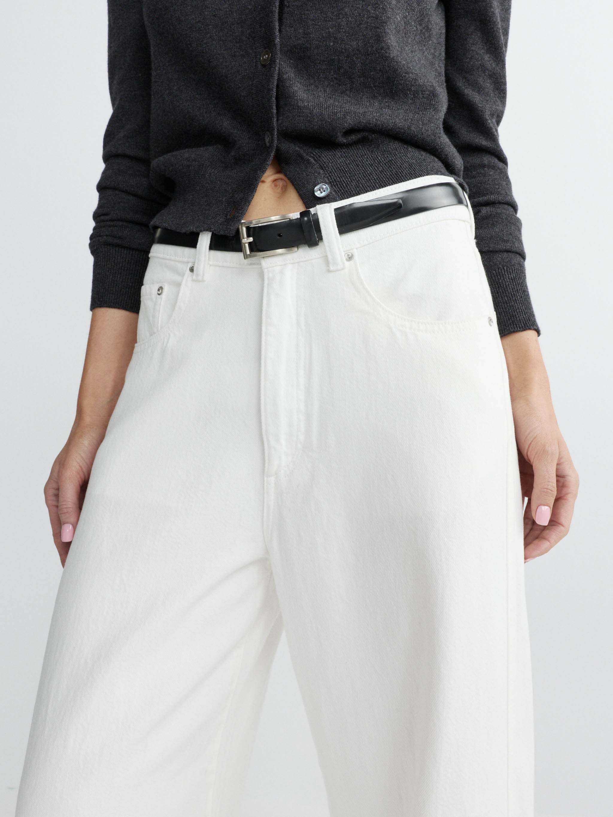 Person wearing a dark sweater and white pants with a black belt on a light gray background