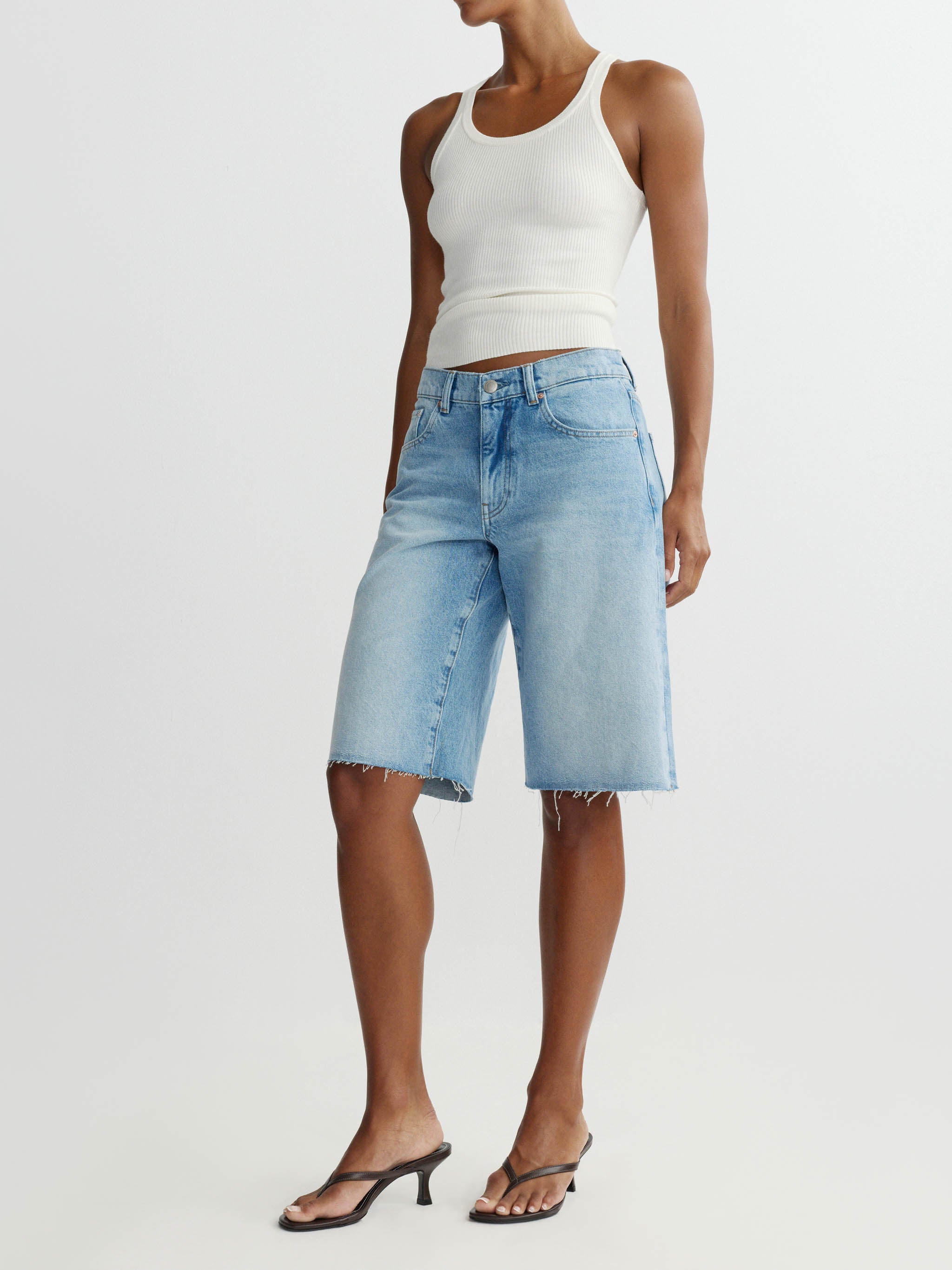 Person wearing light blue denim shorts and a white tank top on a plain background