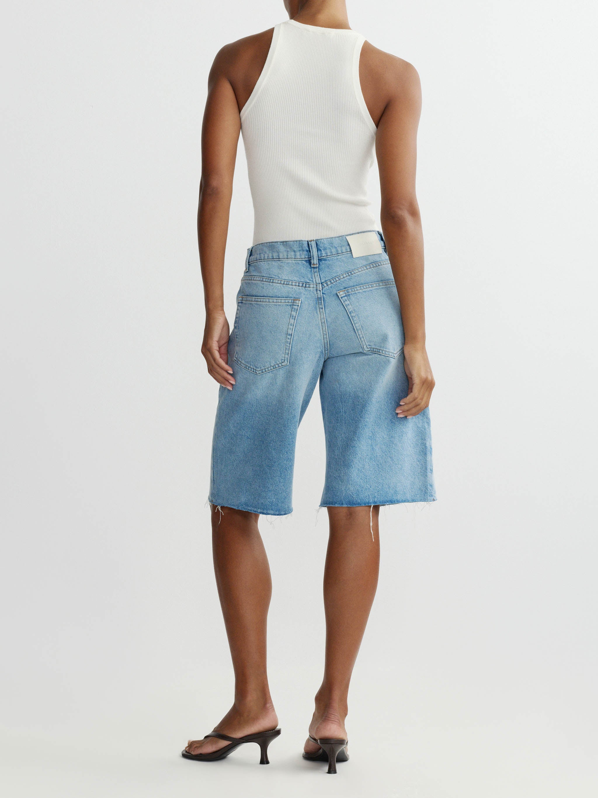 Person wearing a white sleeveless top and light blue denim skirt on a white background