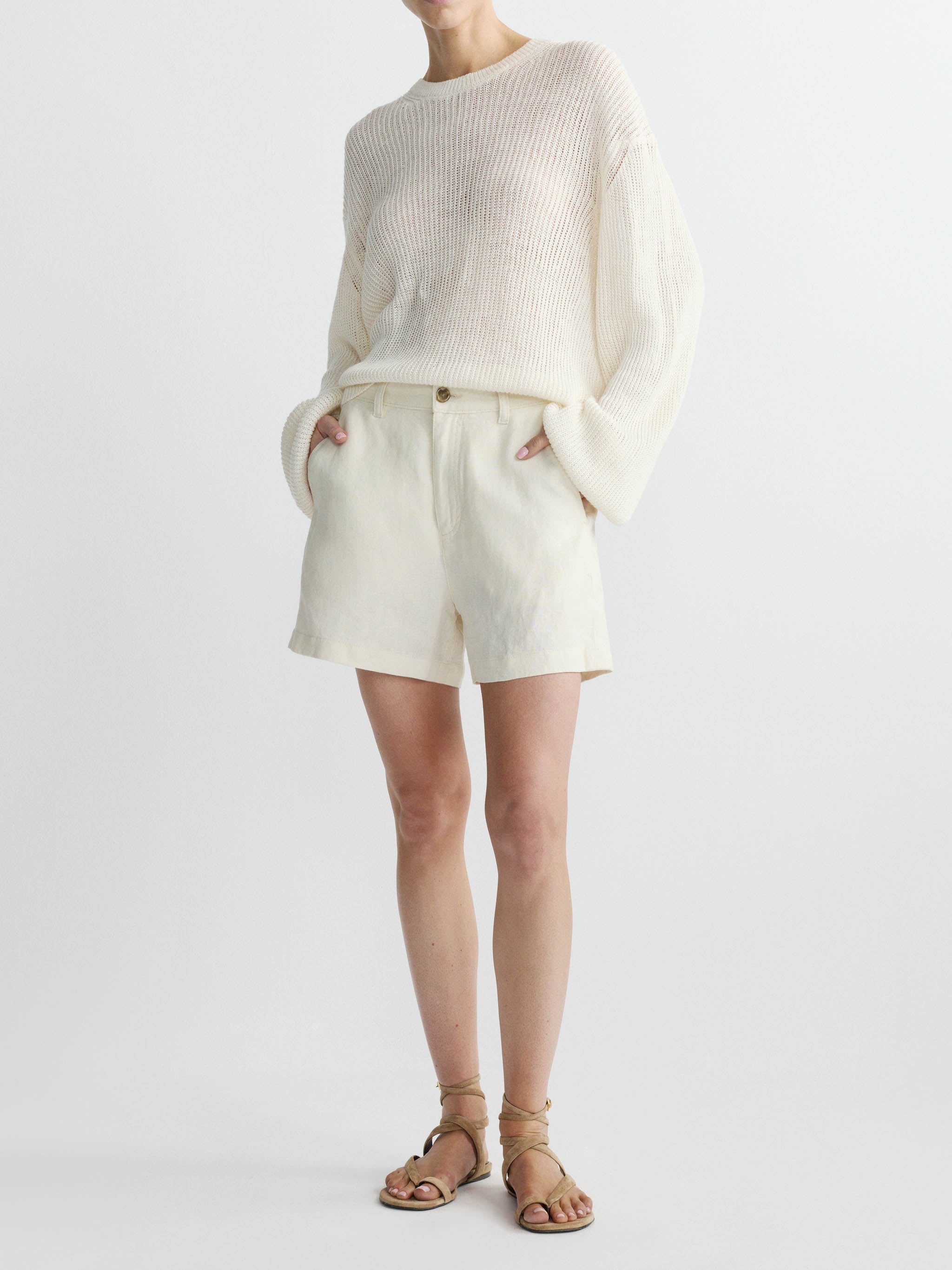 Person wearing a cream sweater and linen shorts set on a white background