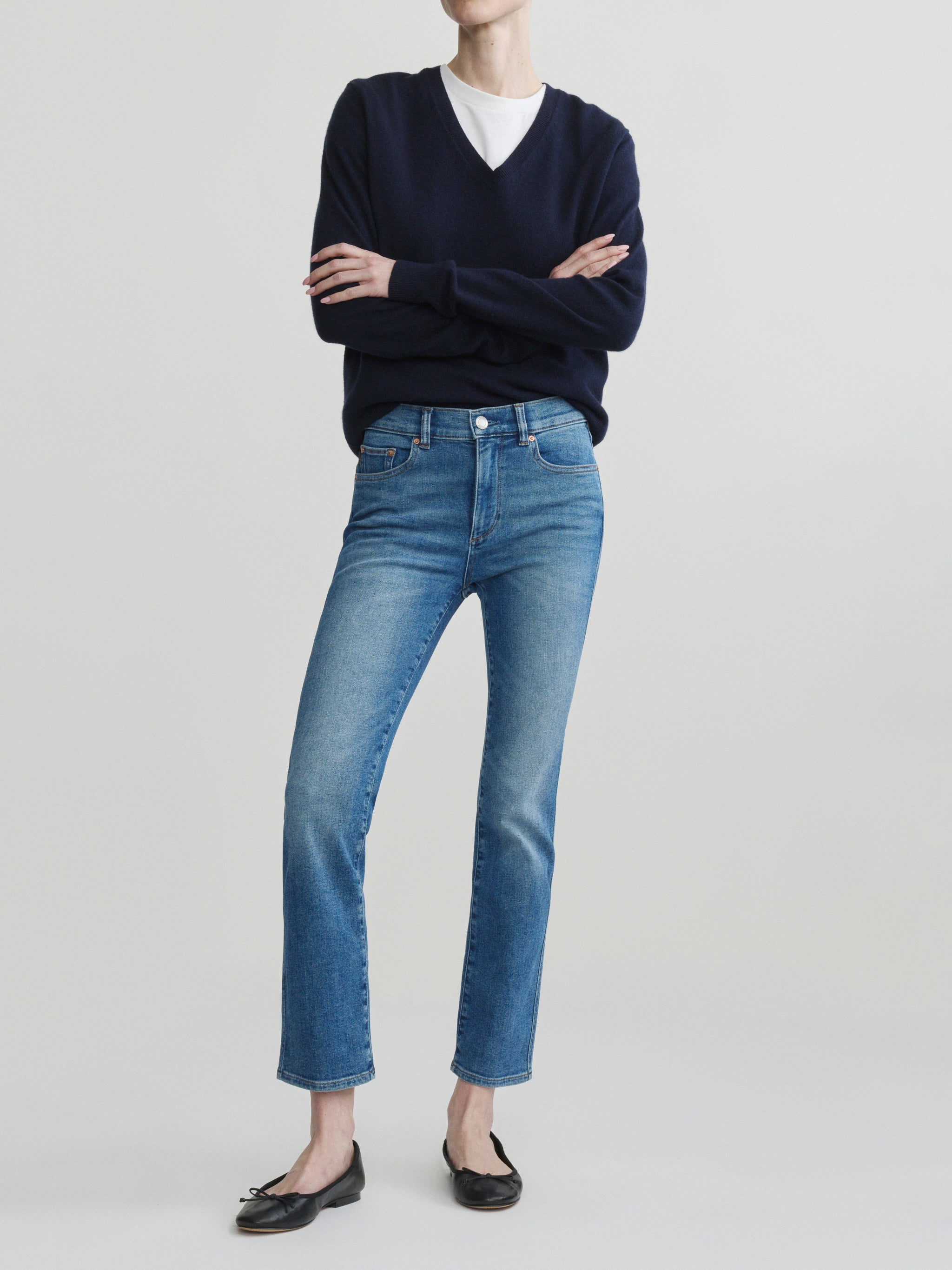 Mara Straight jeans in Crisp Air with a navy sweater on a model, full-length front view, arms crossed.