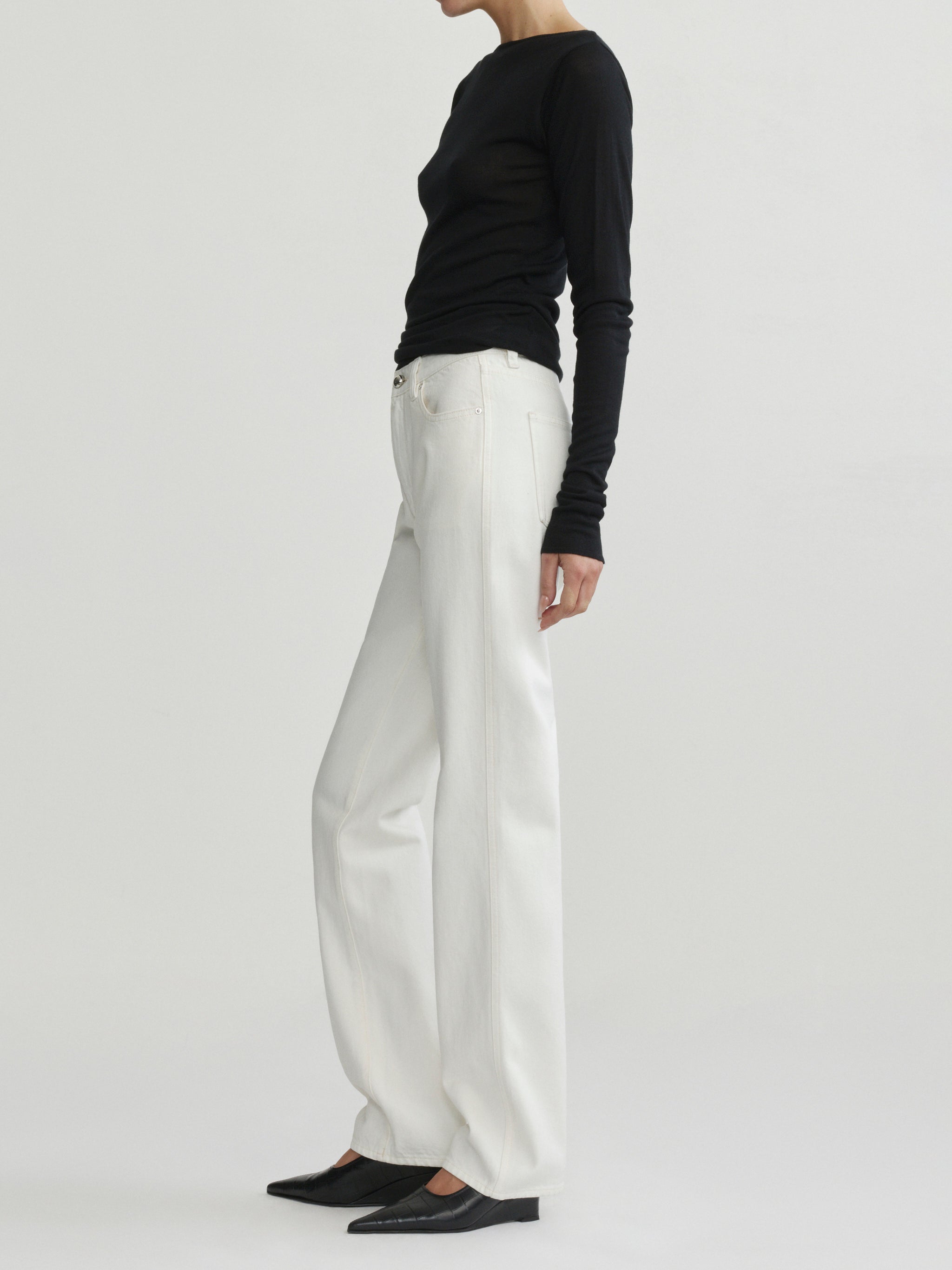 Cate Slim Leg jeans in Eggshell with black top on a model, full-length side view in studio.