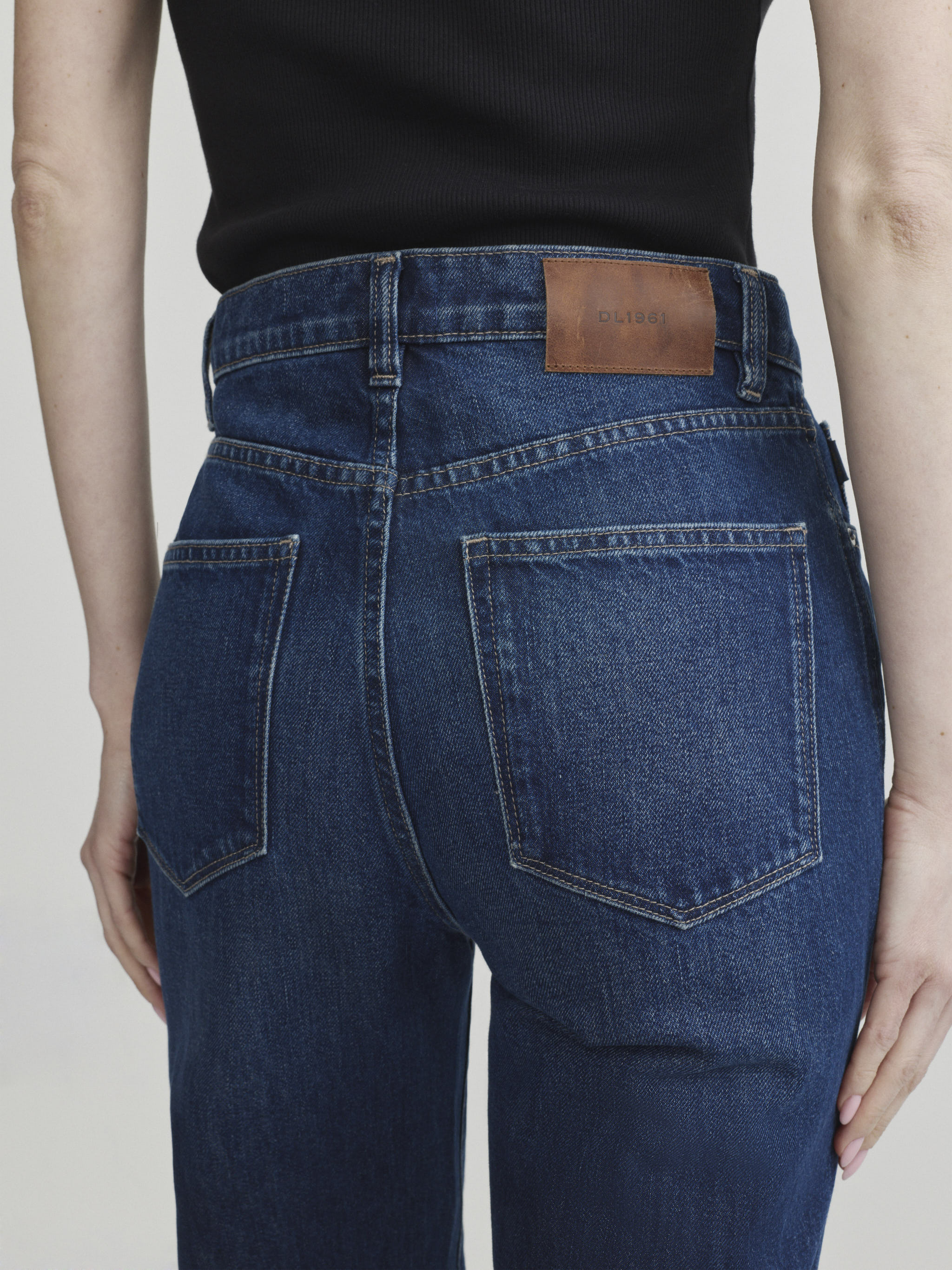 Cate Slim jeans in December on a model with black top, close-up back view of high-rise waist and pockets.