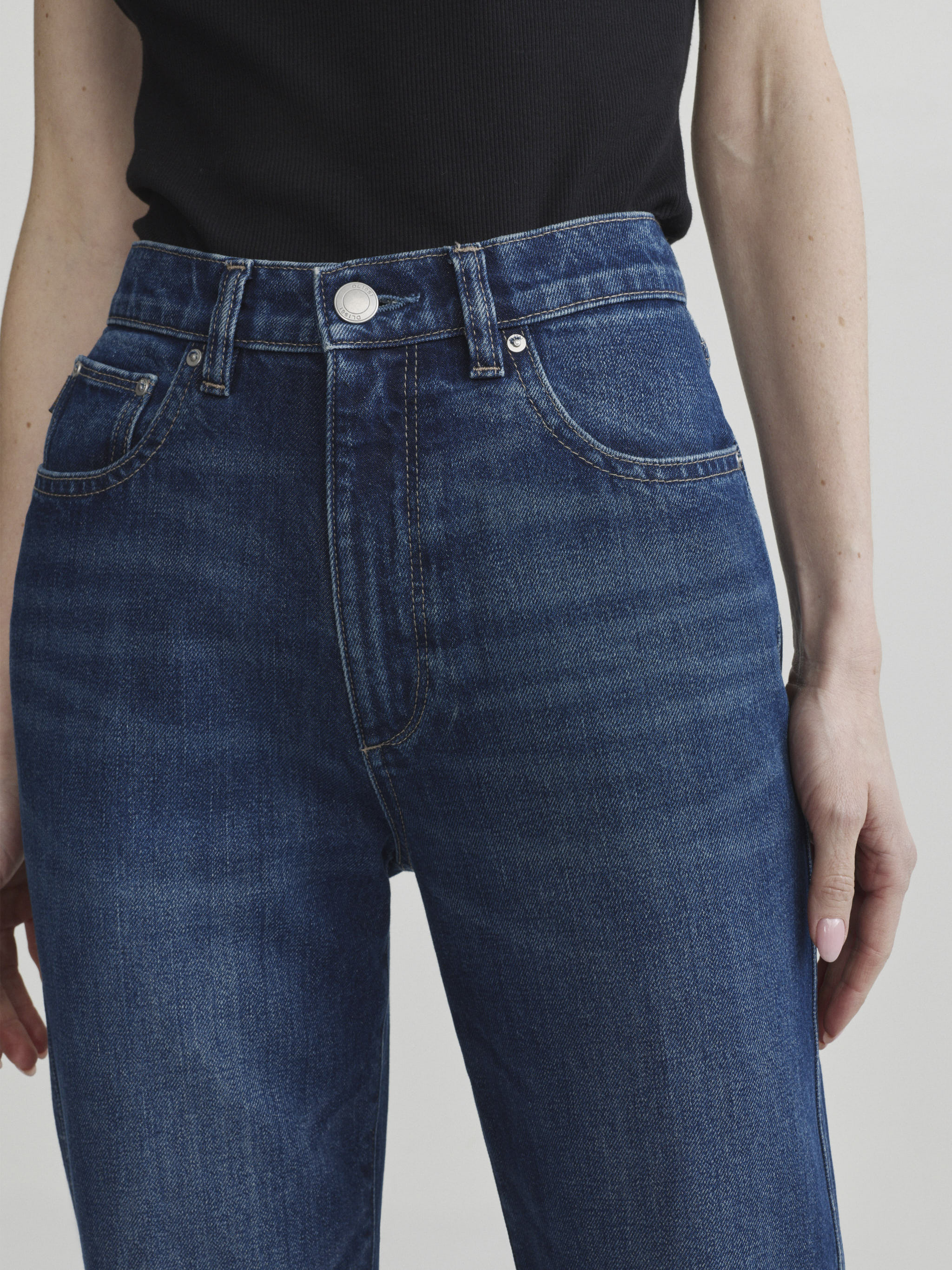 Cate Slim jeans in December on a model with black top, close-up front view of high-rise waist in studio.