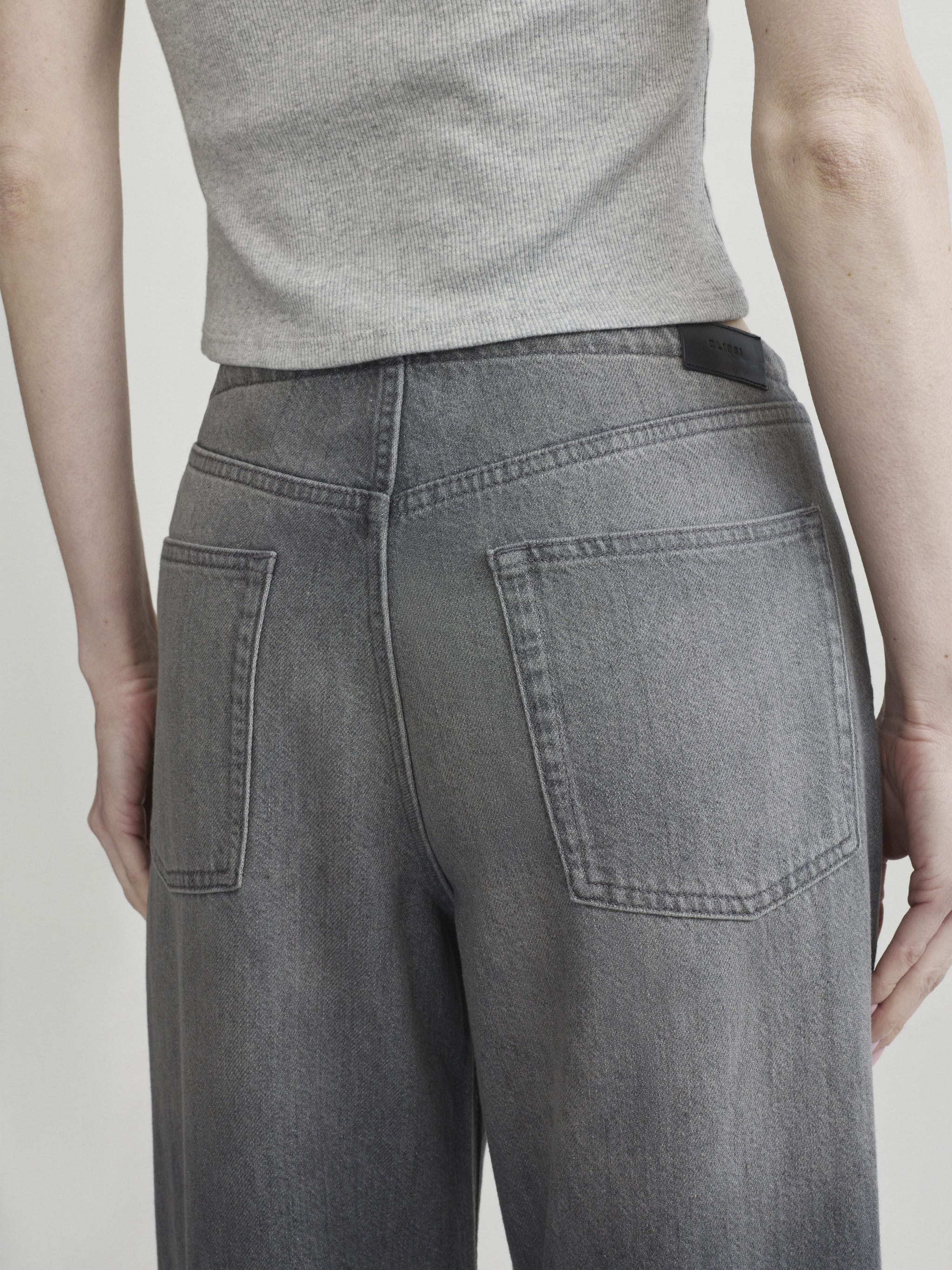Sienna Low-Slung Wide Leg jeans in Ash Grey Aura on a model with grey top, close-up back view of pockets.