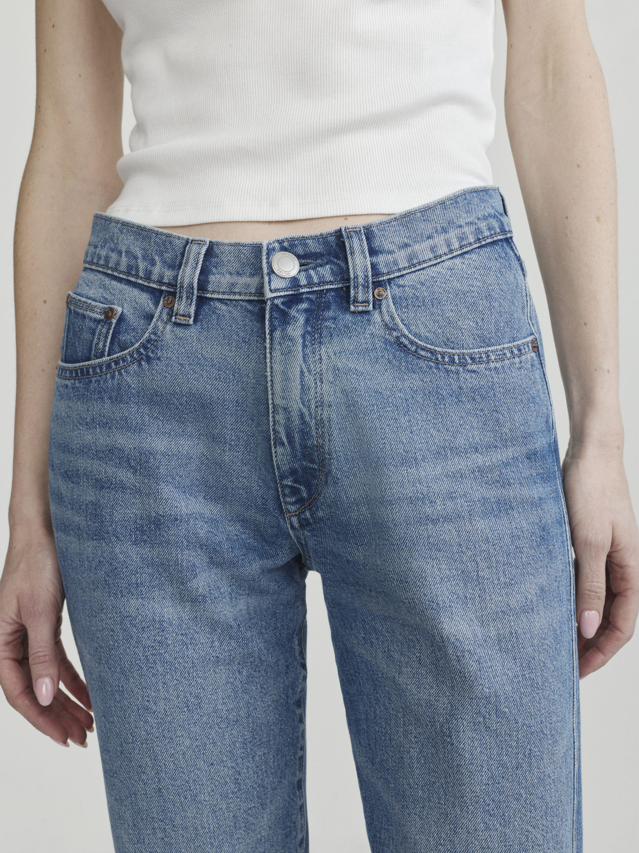 Dakota Slim Straight in Endless Sea on a model with white tank, studio close-up of the waist and hips.