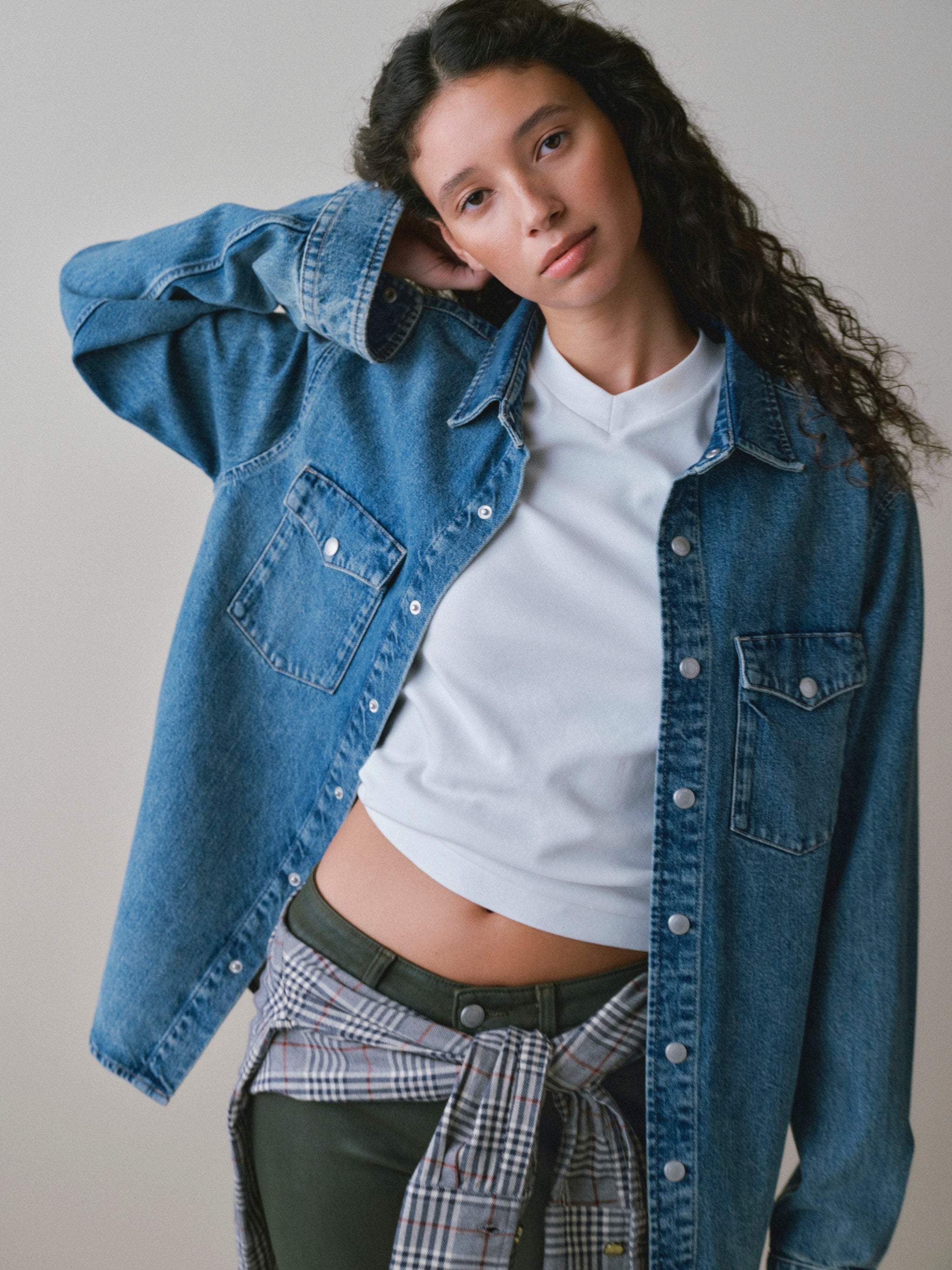 DL1961 women's Shrunken V-neck tee in white, worn under an oversized denim shirt with coated olive jeans.