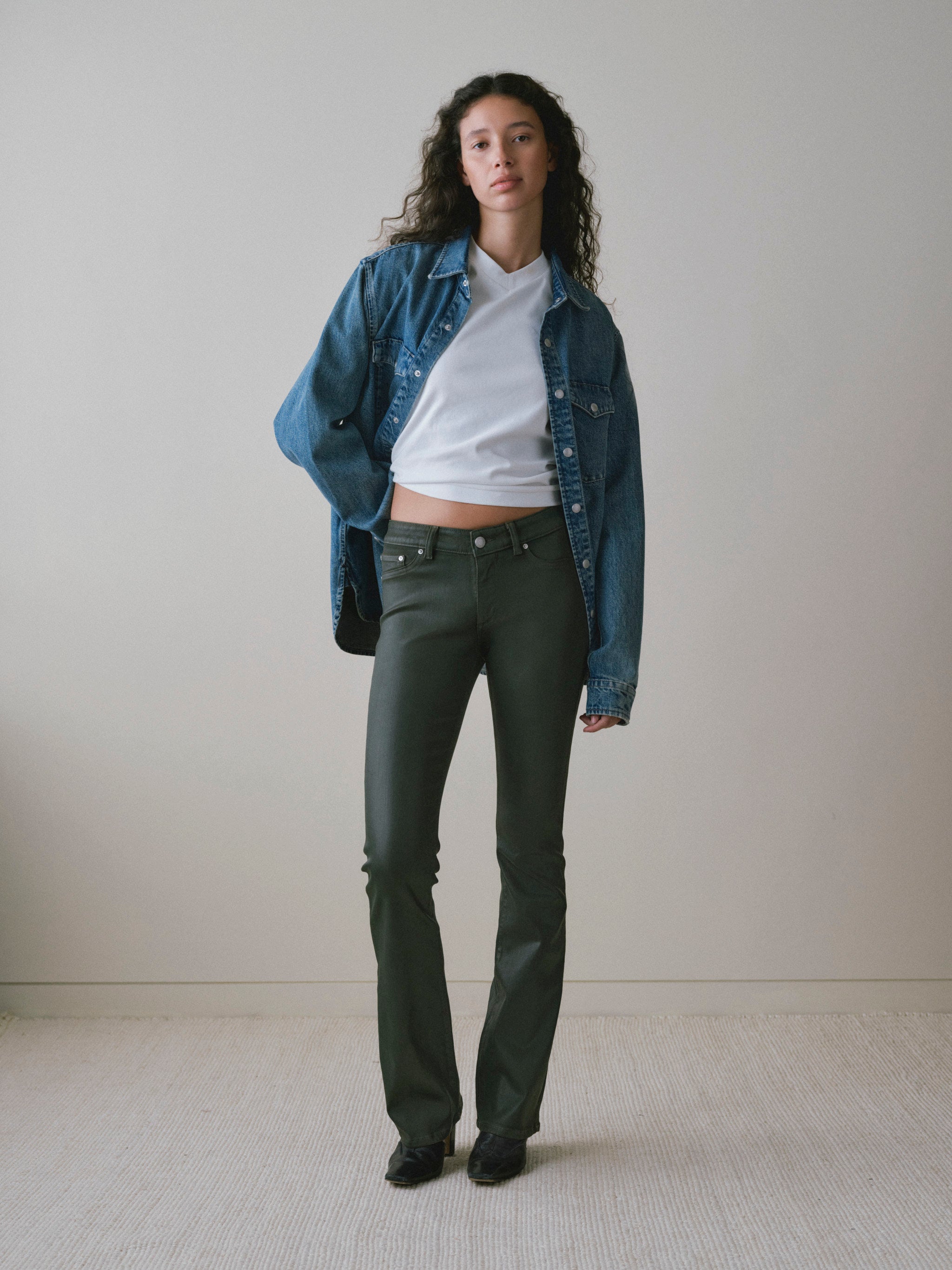DL1961 women's Shrunken V-neck tee in white, full-length front view with a denim jacket and coated olive jeans.