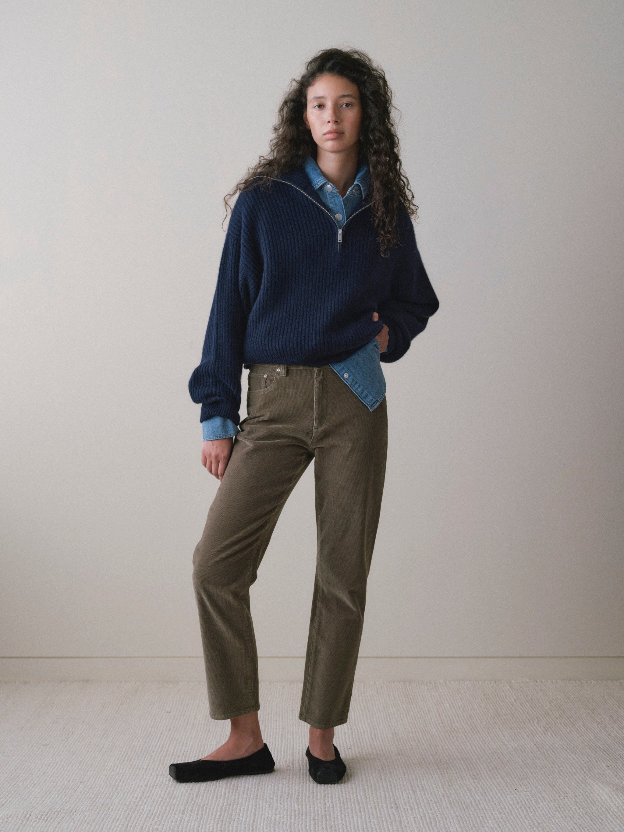 DL1961 women's Cate Stretch Straight High-Rise pants in olive corduroy 'Pine Cord', front view with a navy sweater over a denim shirt.