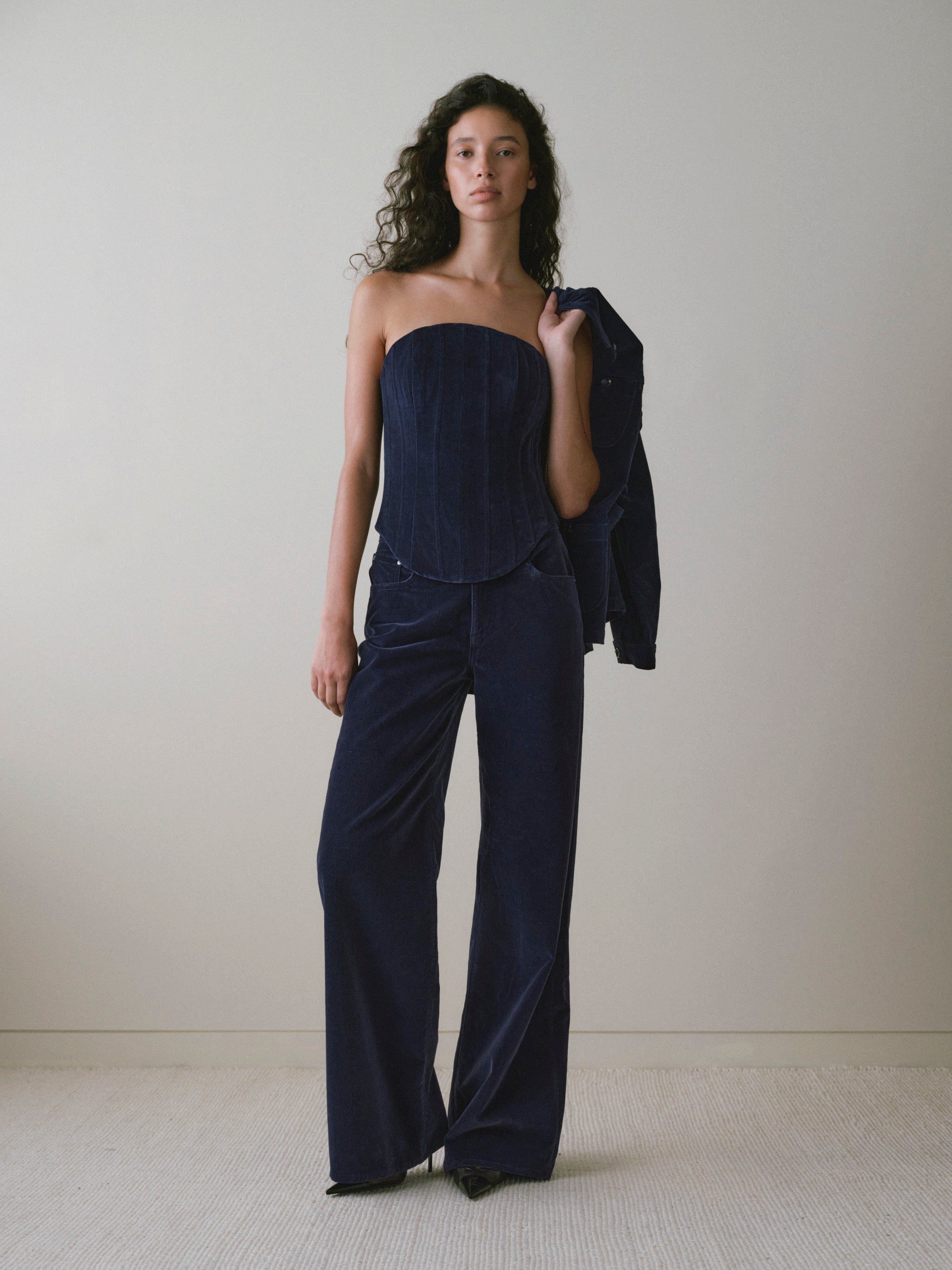 DL1961 women's Utility velvet jacket in navy 'Ajax Velvet', carried over the arm with a velvet corset top and wide leg pants.