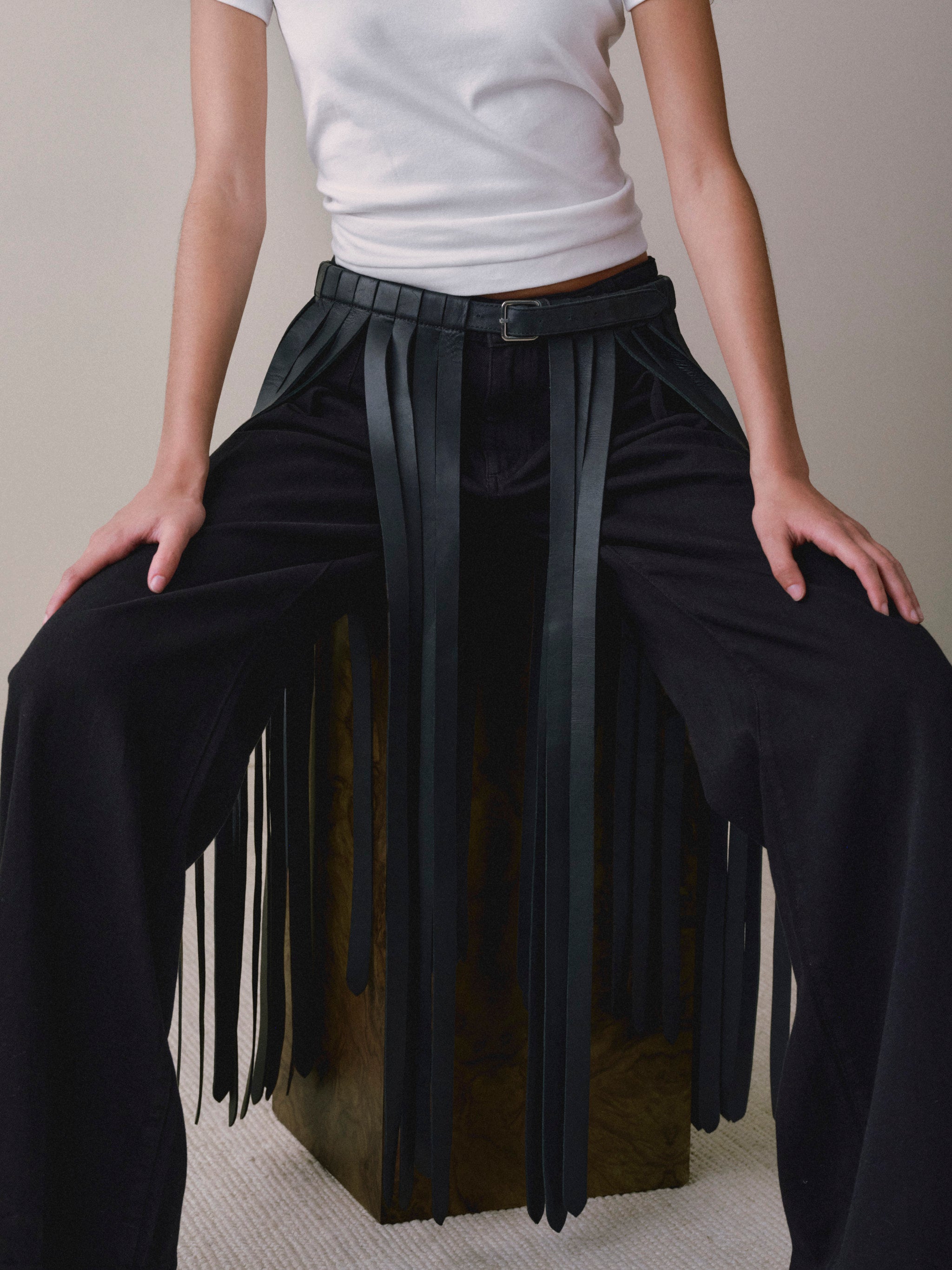 DL1961 fringe leather belt in black, close-up of the buckle and fringe panels over black pants.
