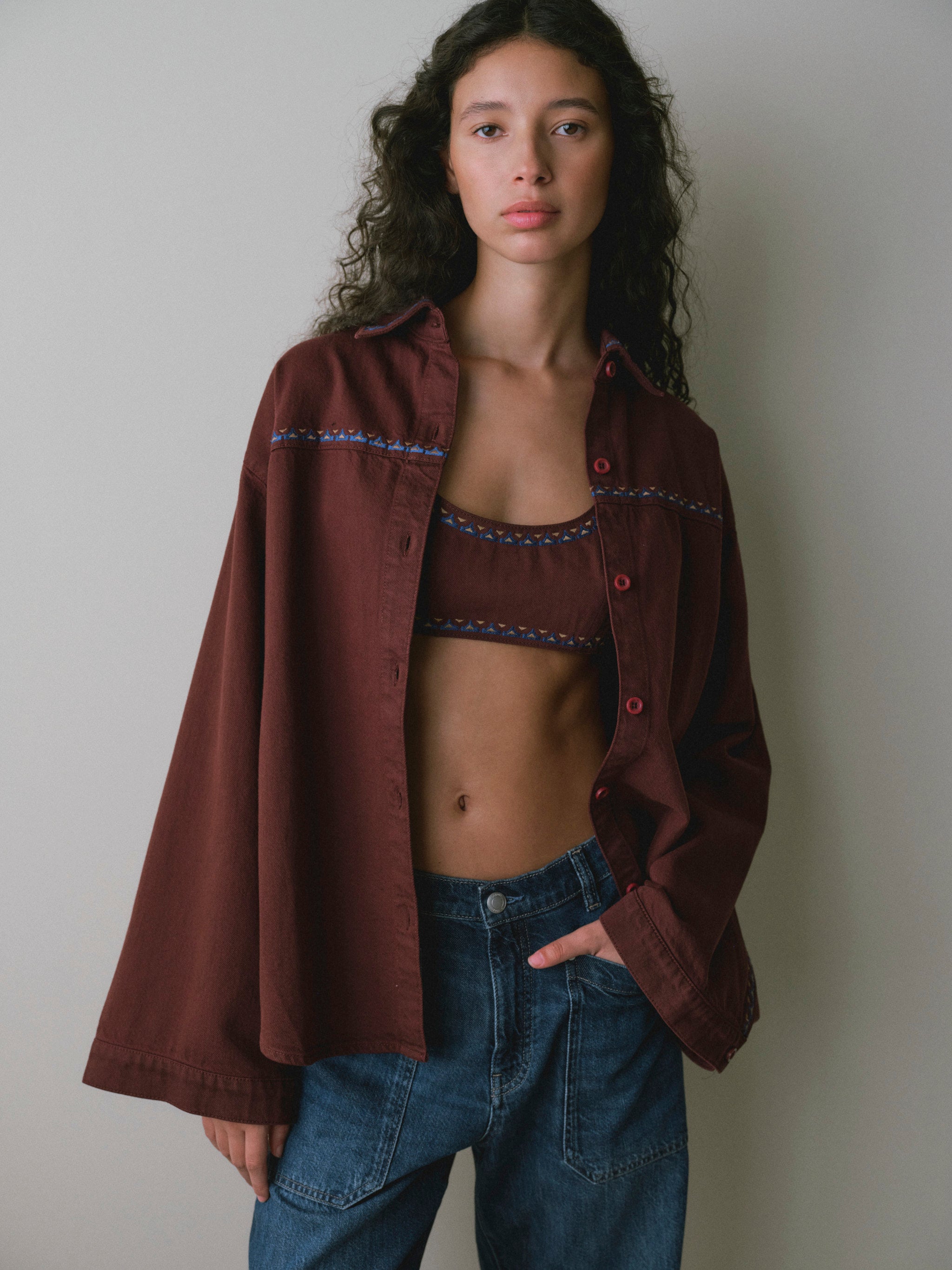 DL1961 women's Colette denim bralette in 'Burgundy Embroidery', front view worn under an open burgundy overshirt with blue jeans.