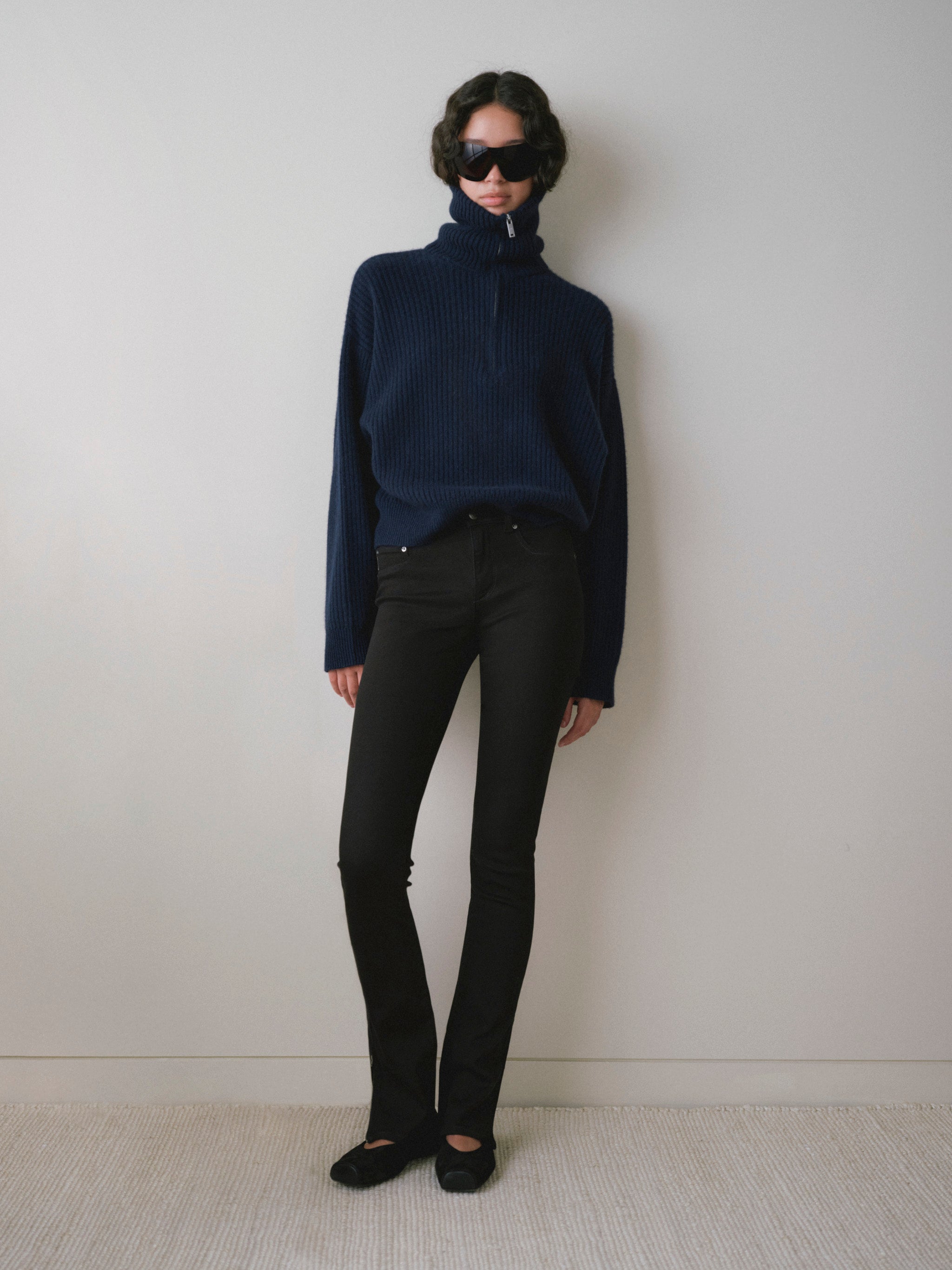 DL1961 women's Jessica Skinny Low-Rise Instasculpt jeans in black 'Cascade', full-length front view with a navy half-zip sweater.