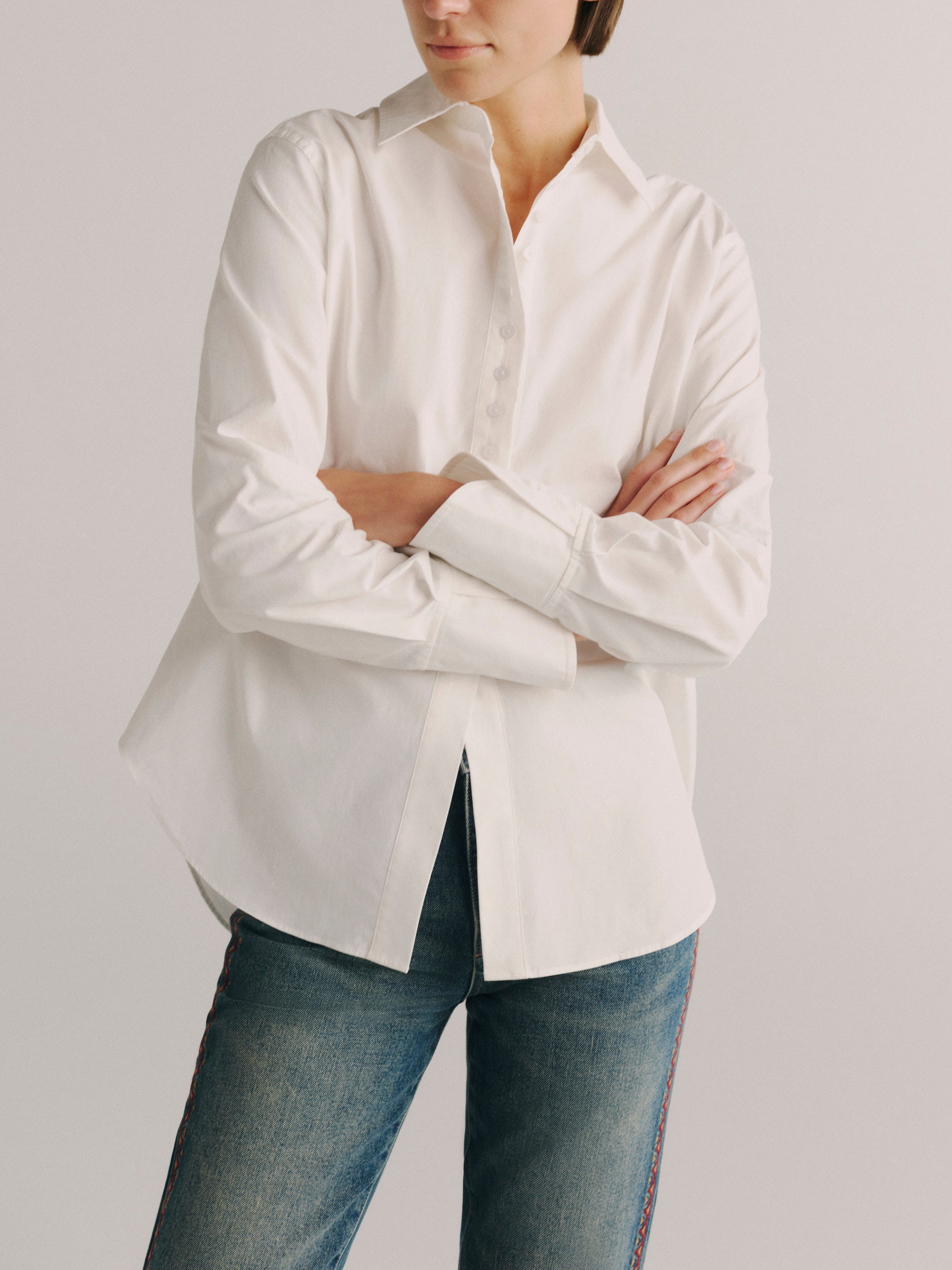 DL1961 women's Kaia poplin shirt in white, front view with arms crossed showing the cuff detail.