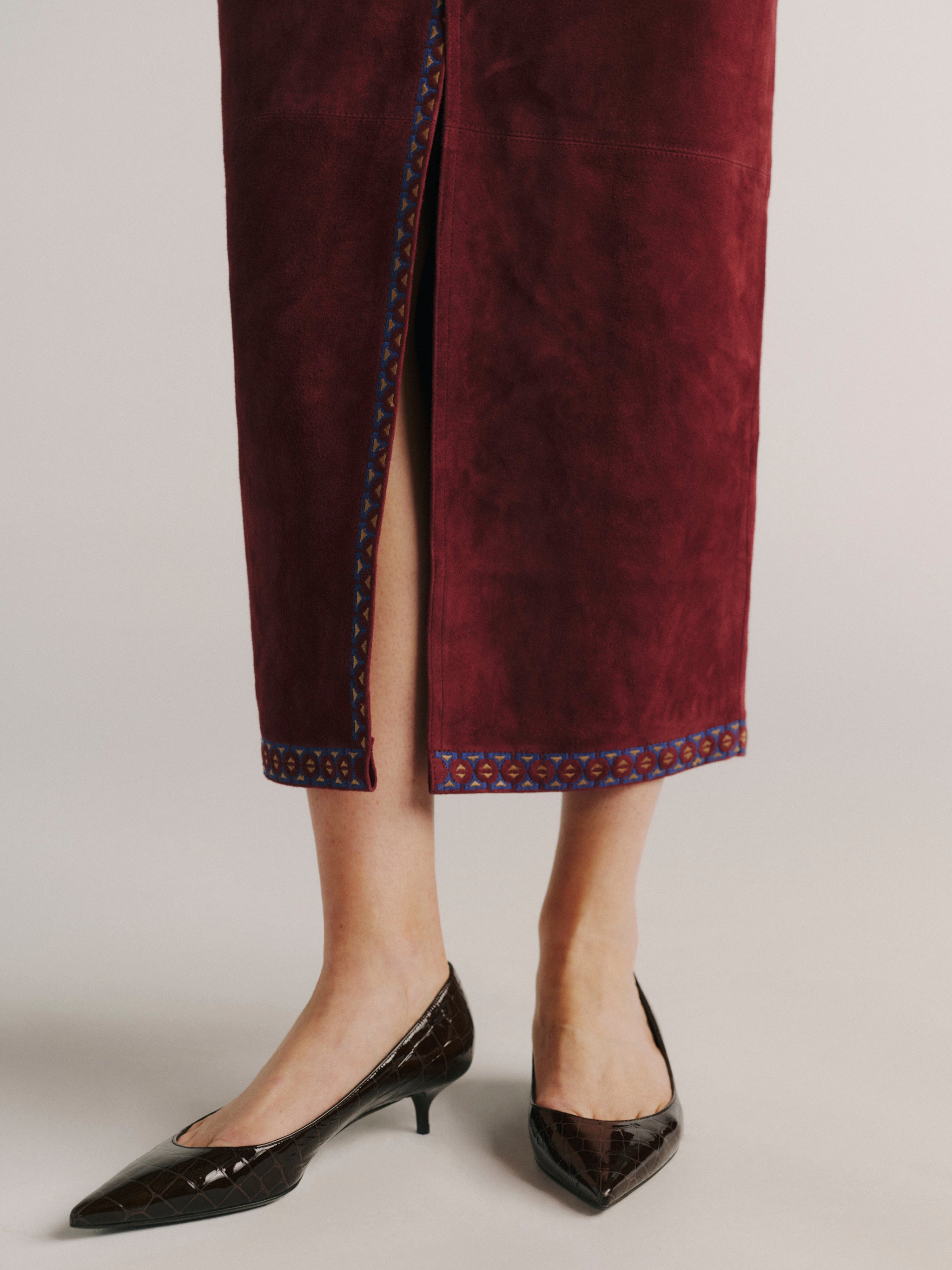 DL1961 women's Alma suede midi skirt in 'Burgundy Suede Embroidery', close-up of the embroidered hem trim and slit.