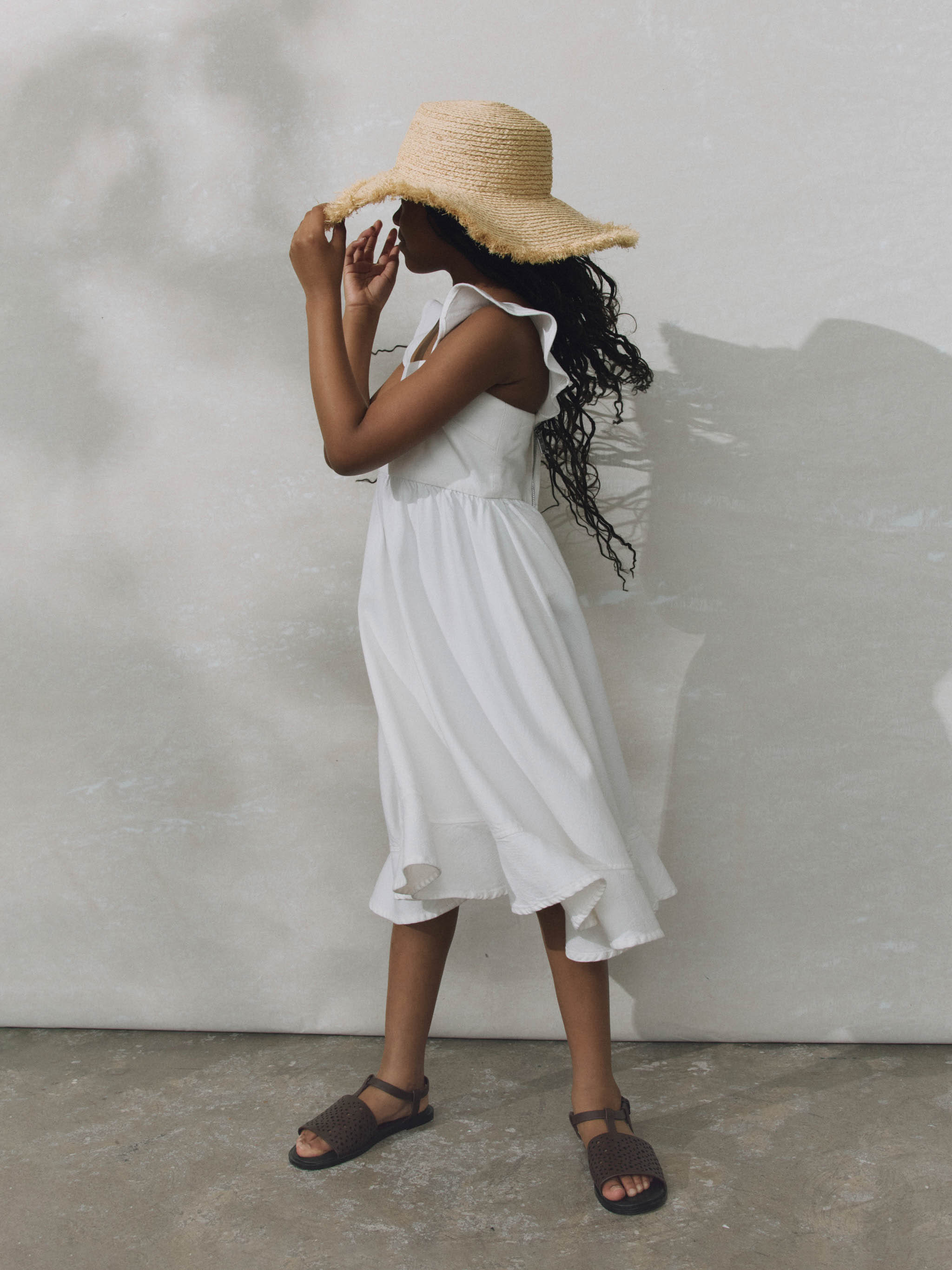 Girl wearing white ruffled dress on plain background.