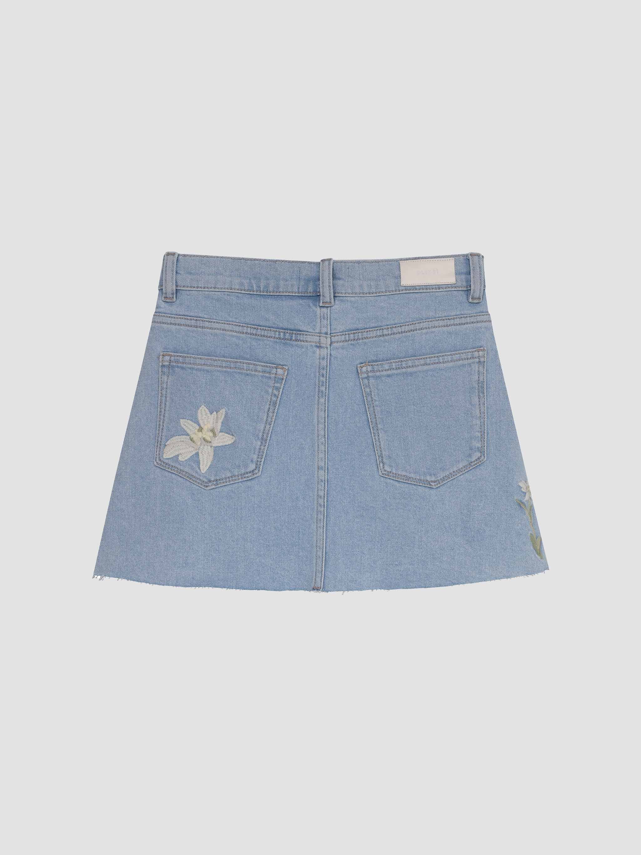 Light blue denim skirt with floral pocket detail on a light gray background
