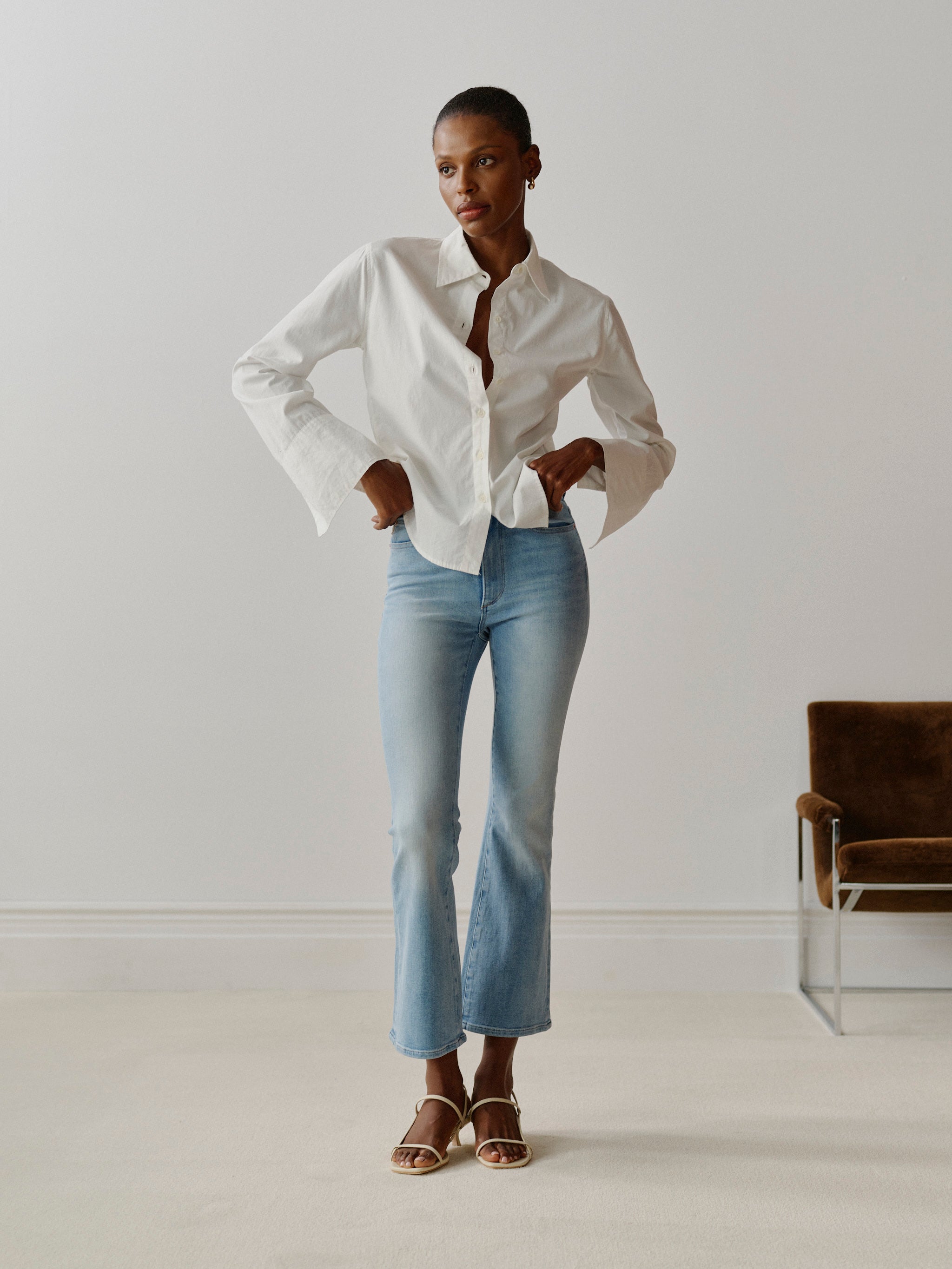 Person wearing a white shirt and light blue jeans standing in a minimalistic room.