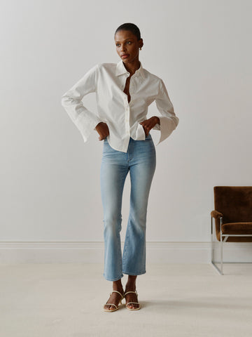 Person wearing a white shirt and light blue jeans standing in a minimalistic room.