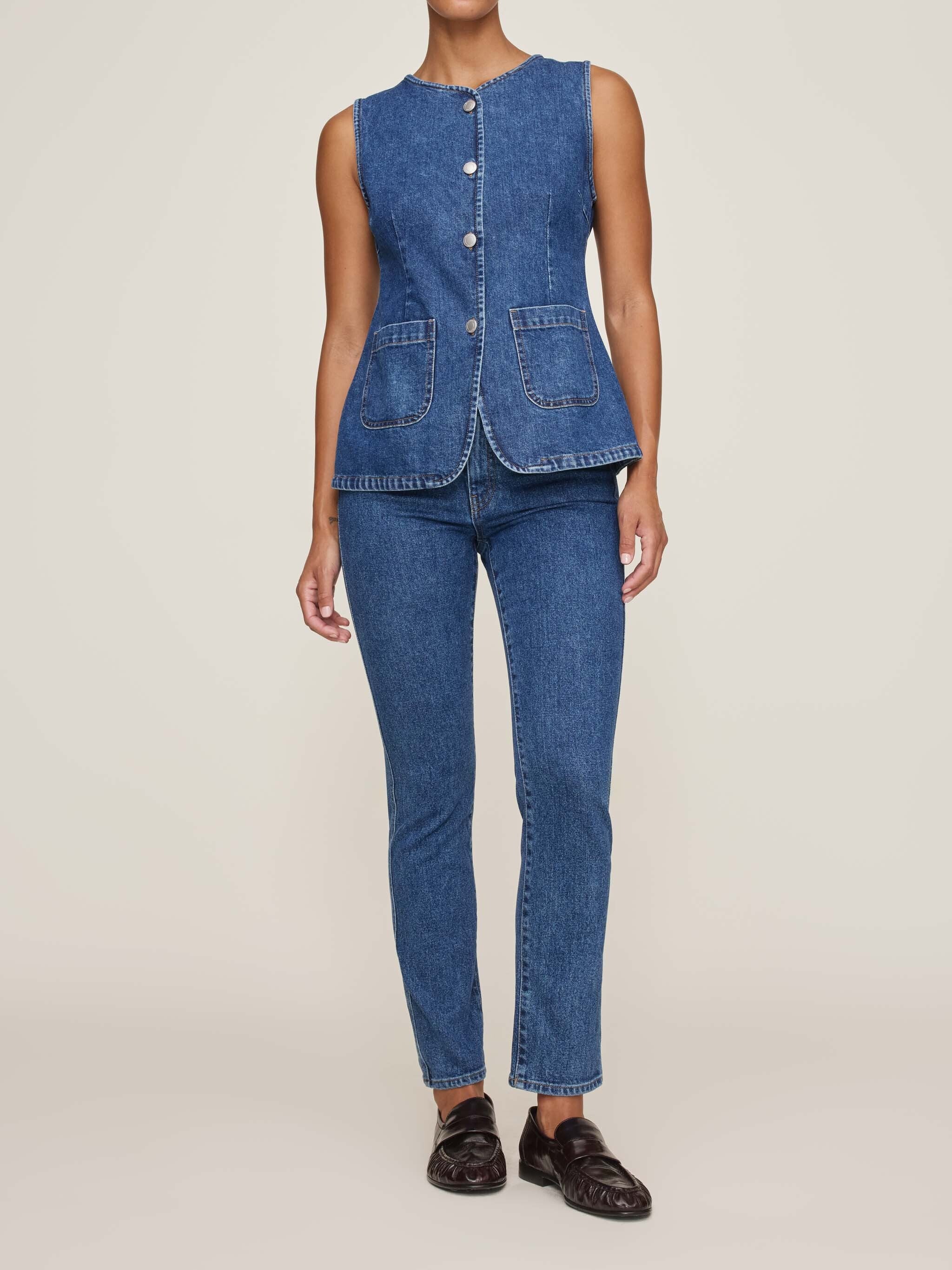 Person wearing a blue denim vest and jeans on a plain background