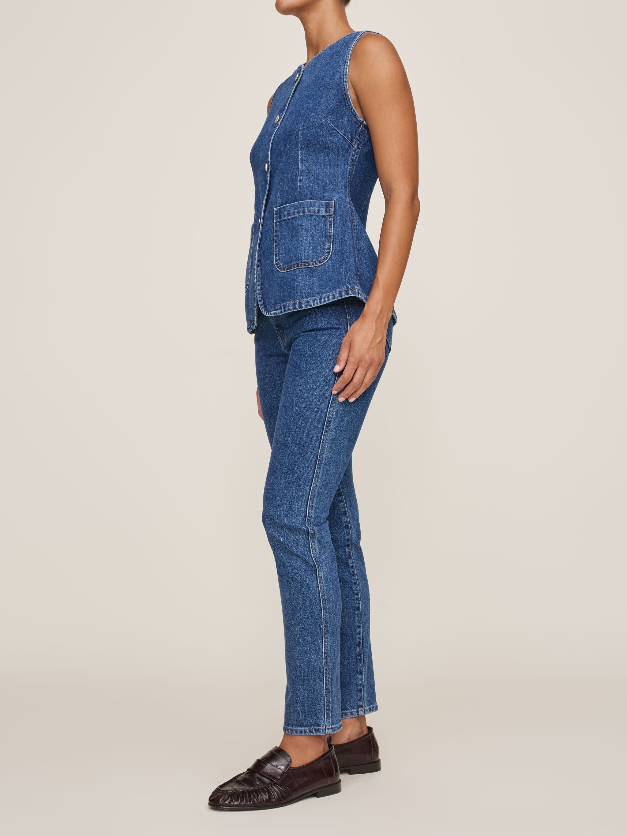 Person wearing a blue denim vest and jeans on a beige background