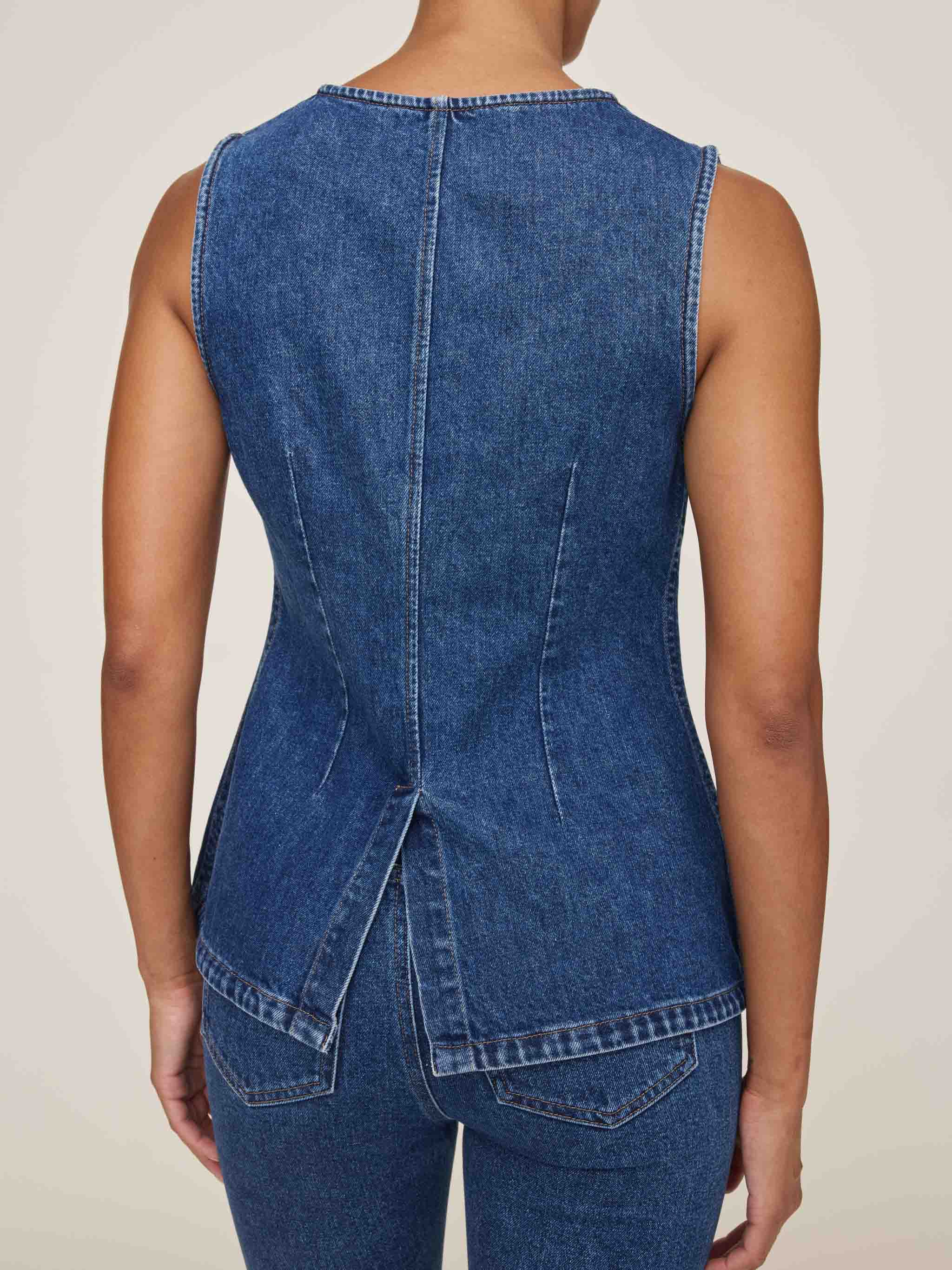 Blue denim sleeveless top on a person against a neutral background