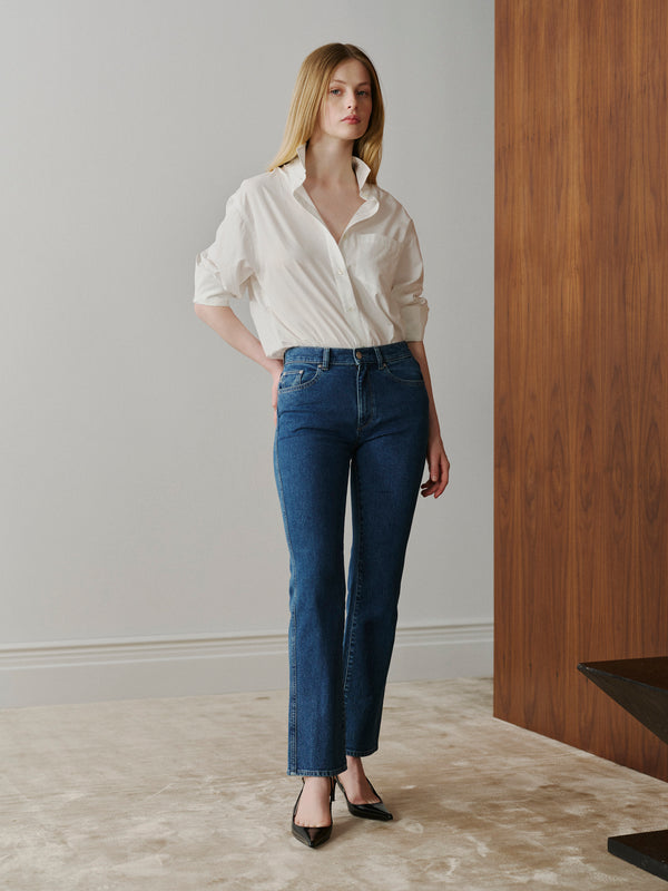 Woman wearing a white shirt and blue jeans standing in a room with wooden paneling.