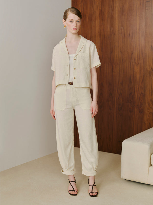 Woman wearing a beige outfit standing in a minimalistic room with a wooden wall.