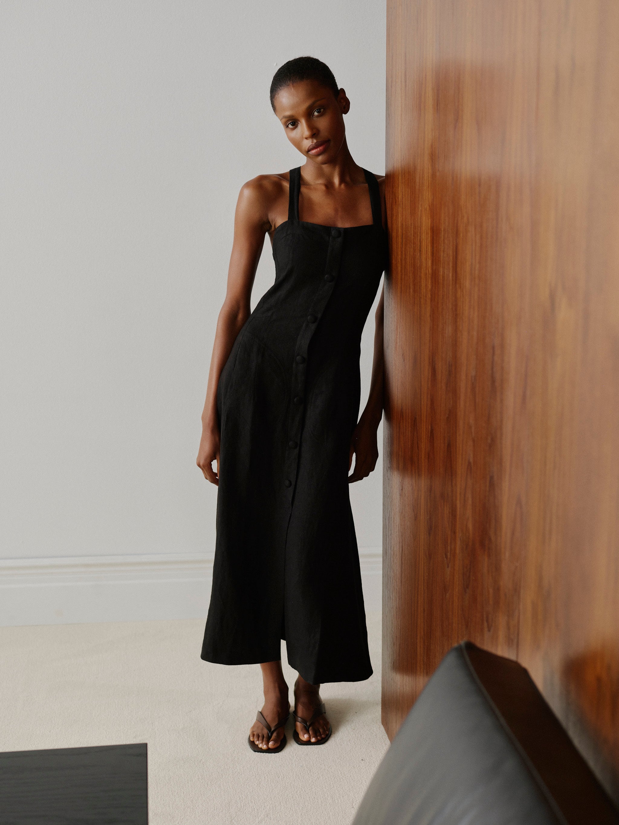 Woman wearing a black dress standing in a minimalistic room.