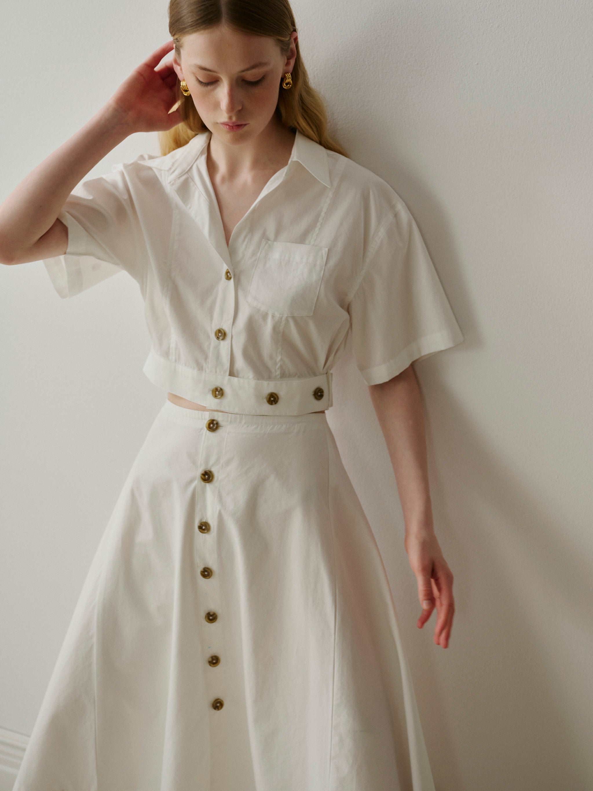 Woman wearing a white outfit with brown buttons against a plain background