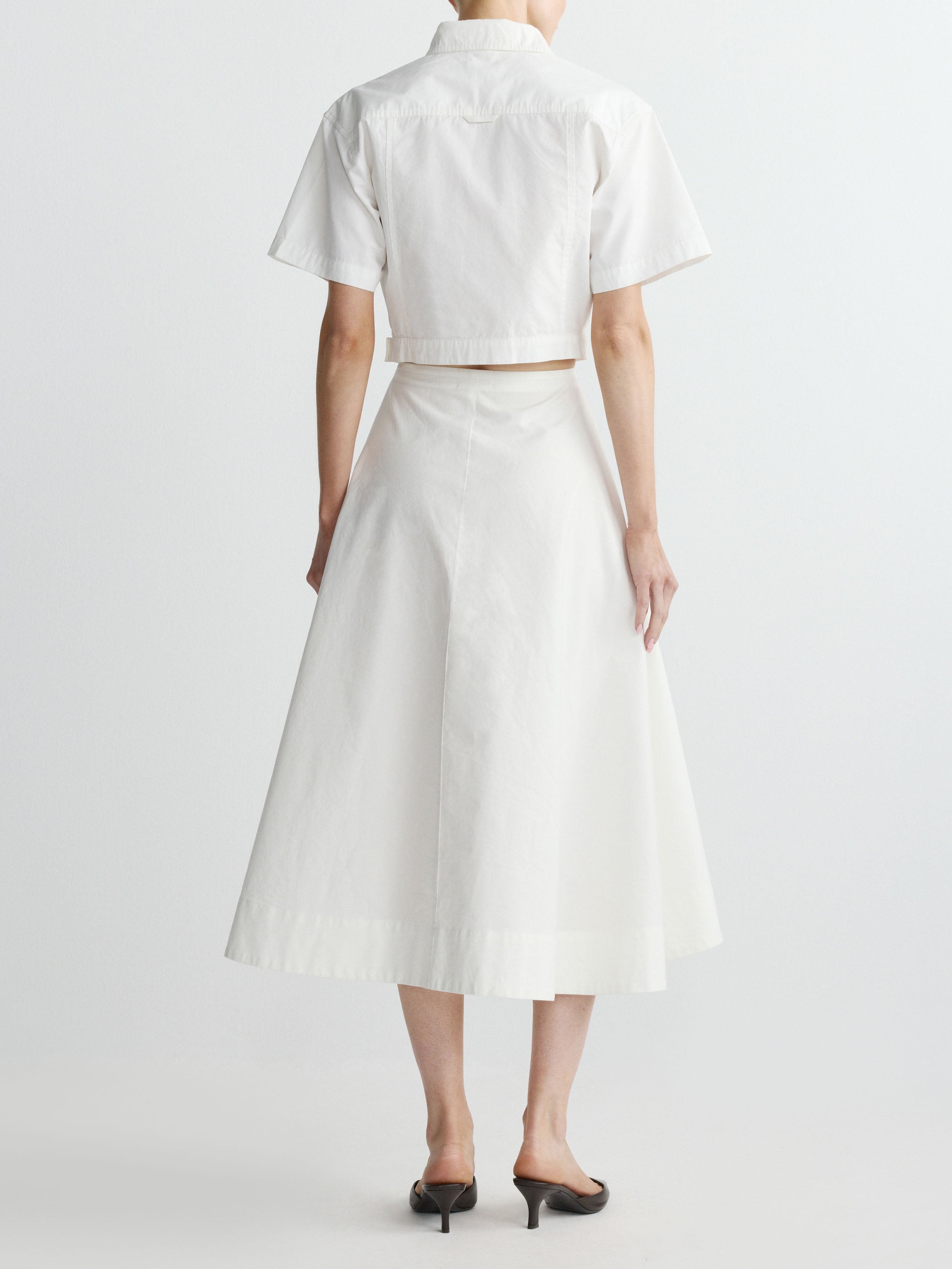 Person wearing a white outfit with a skirt and short-sleeve top on a plain background