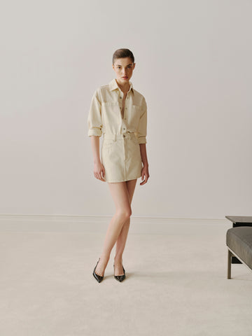 Person wearing a beige shirt and skirt in a minimalistic setting