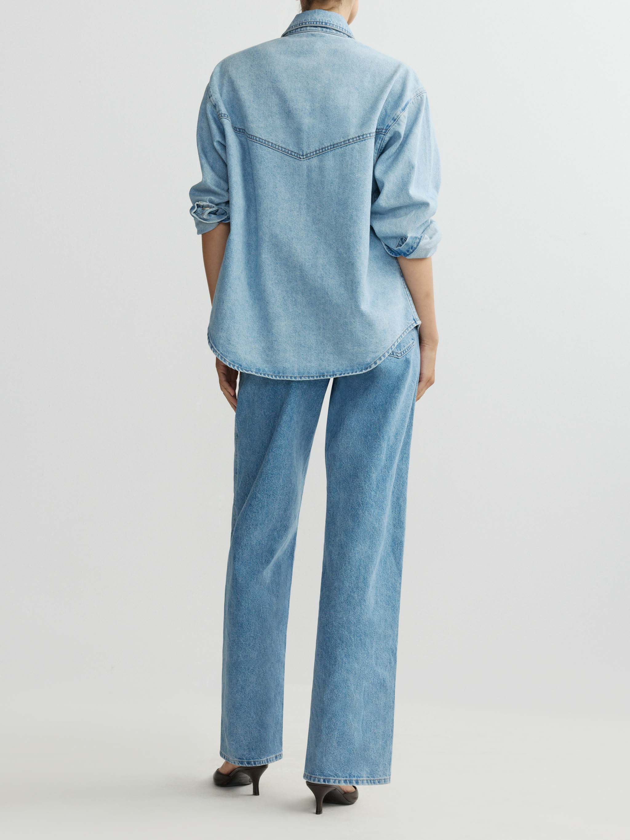 Person wearing a light blue denim shirt and jeans on a white background