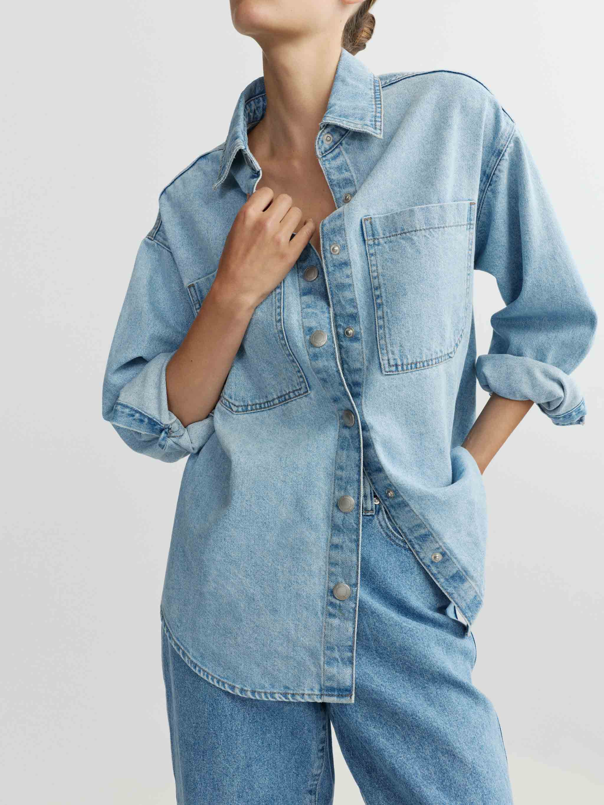 Person wearing a light blue denim shirt and jeans on a plain background