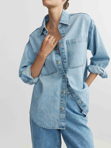 Person wearing a light blue denim shirt and jeans on a plain background