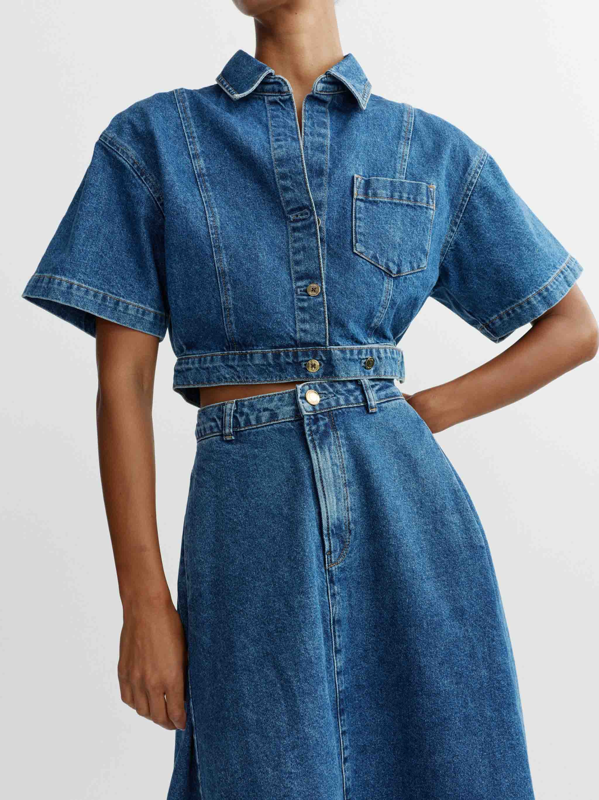 Person wearing a blue denim dress on a plain background
