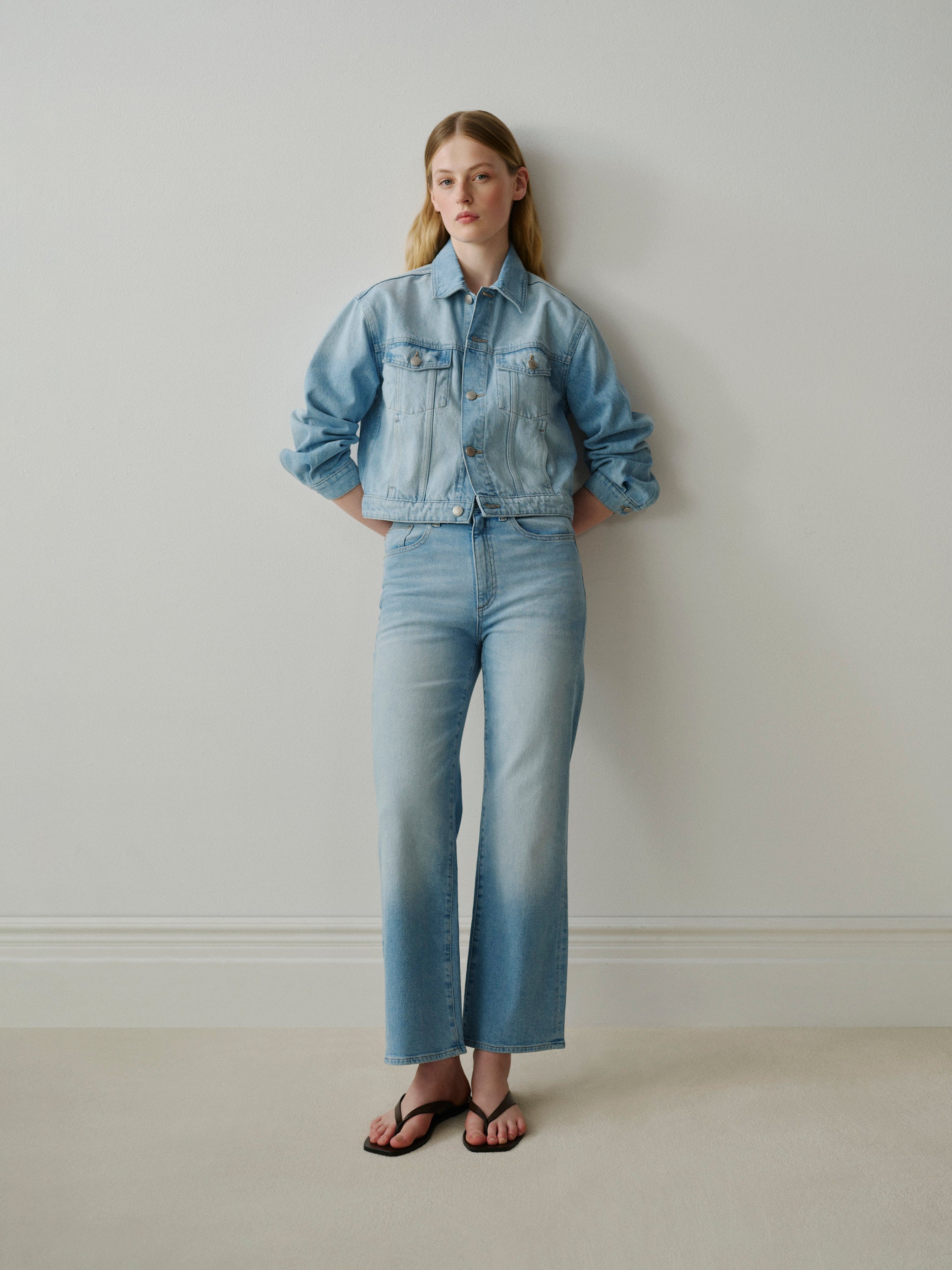 Woman wearing a light blue denim jacket and jeans against a plain background
