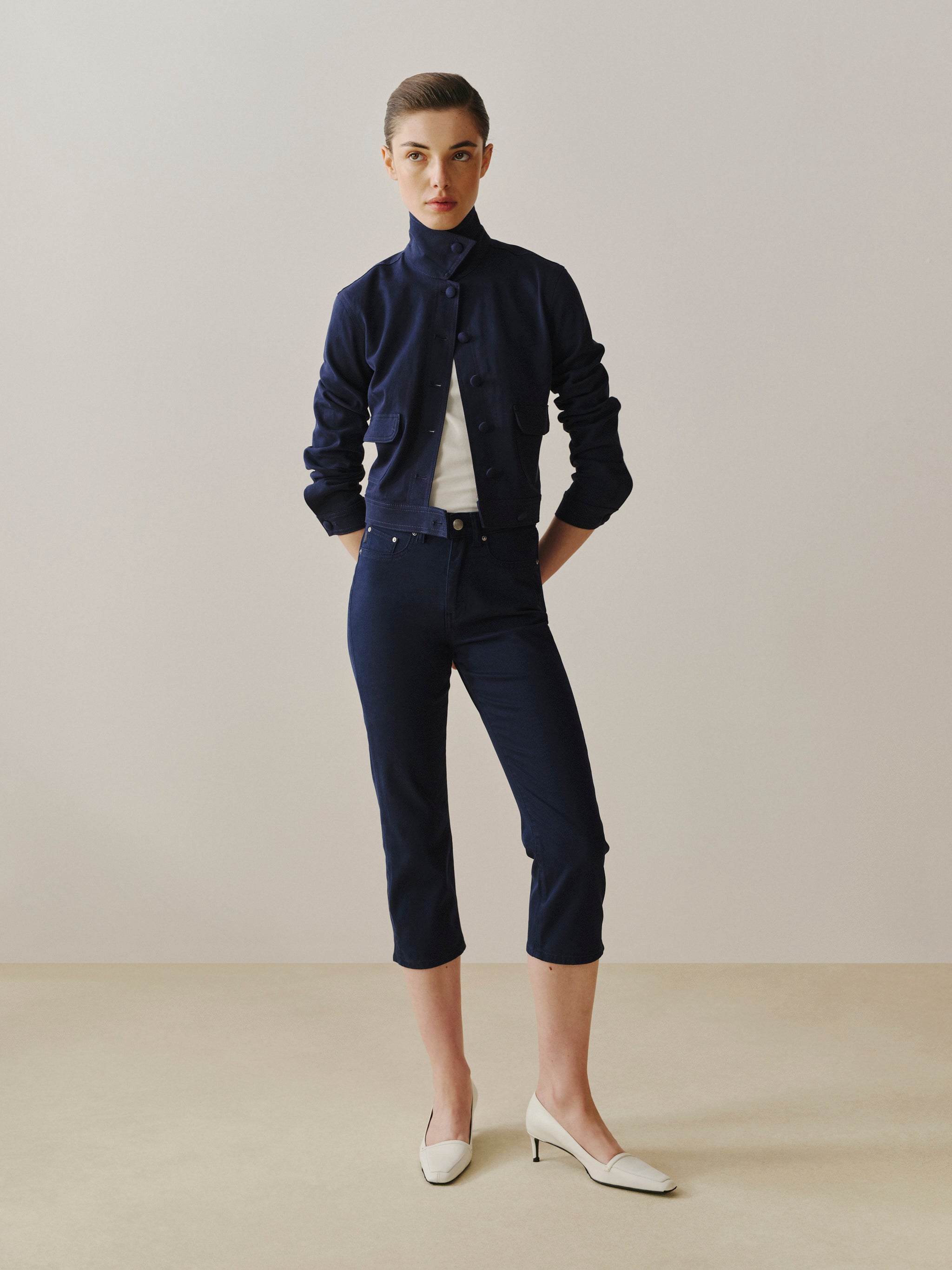 Person wearing a navy blue shirt and pants with white shoes on a plain background