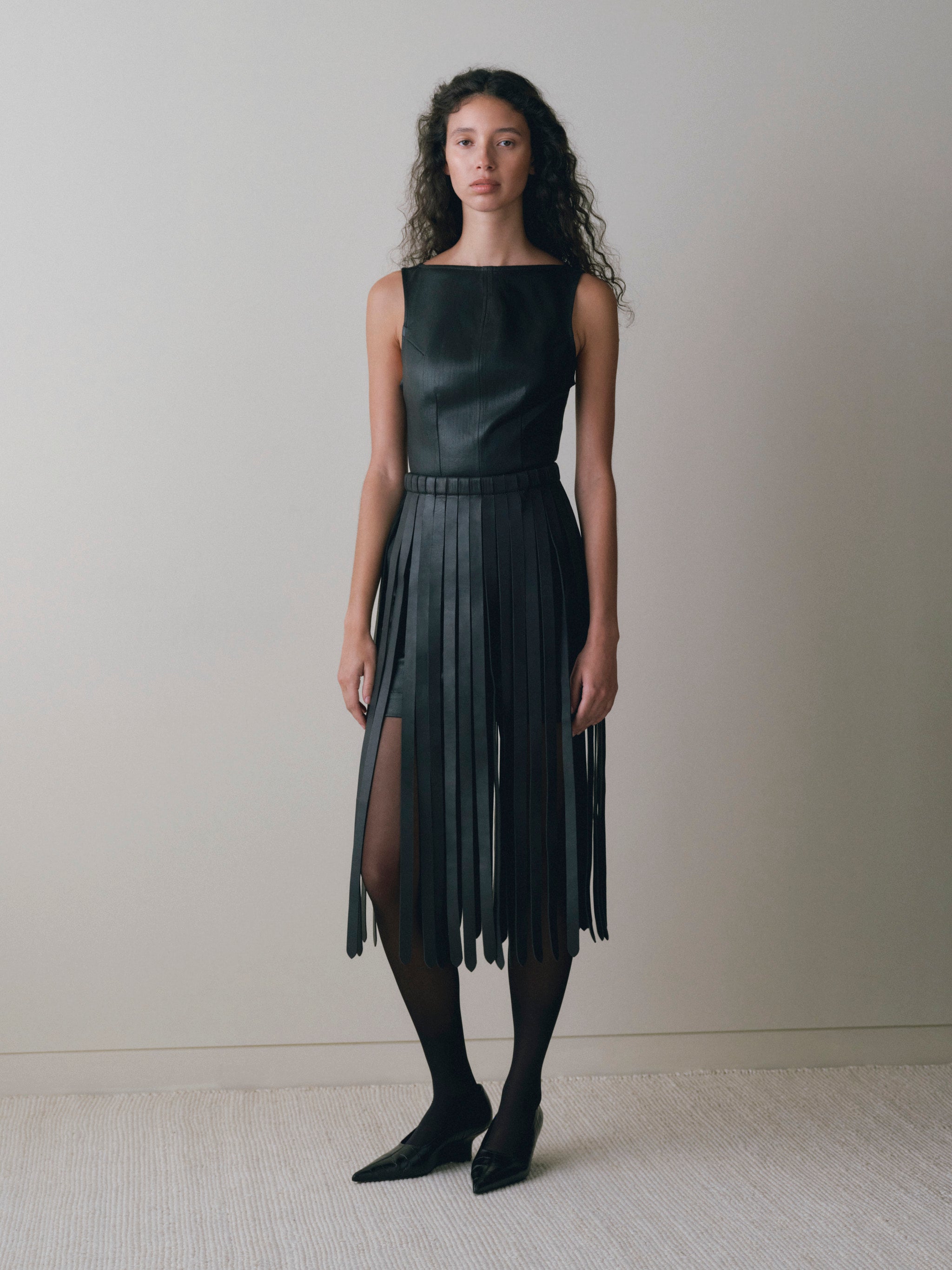DL1961 women's Esme boat neck Instasculpt denim mini dress in 'Black Hawk Coated', front view styled with a black fringe belt and tights.