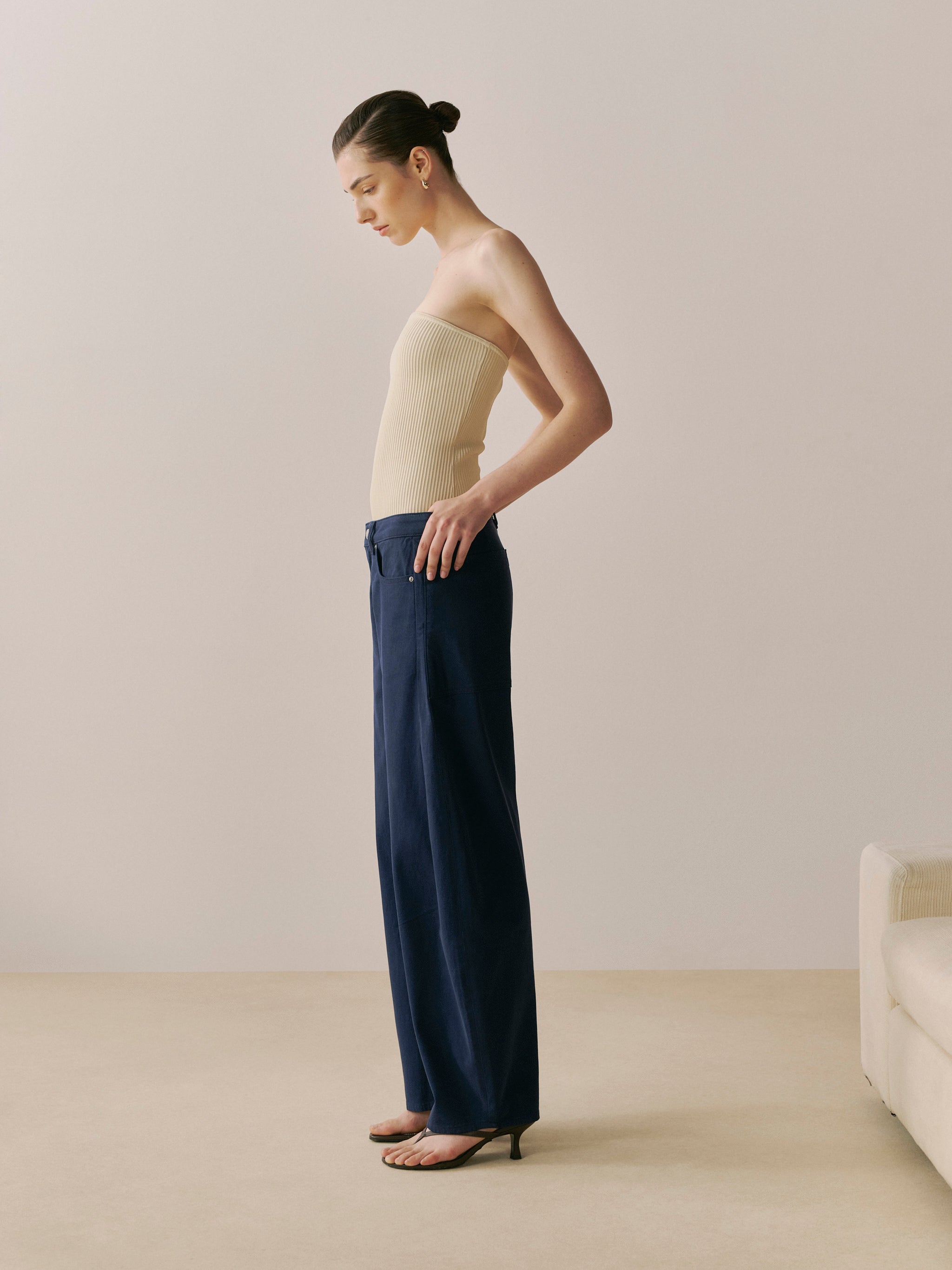 Woman wearing a beige strapless top and navy pants in a minimalistic room.