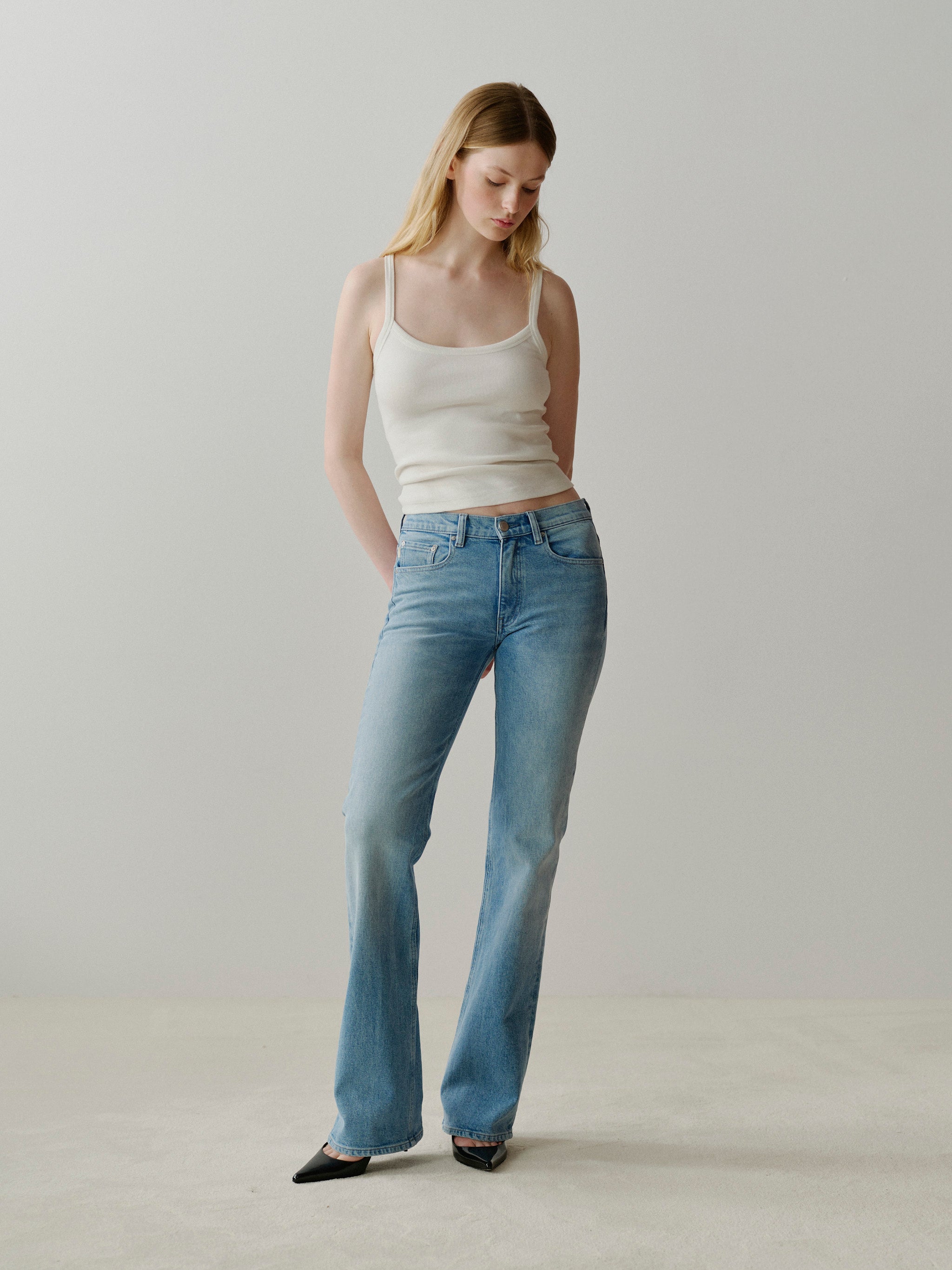 Woman wearing a white tank top and blue jeans against a plain background