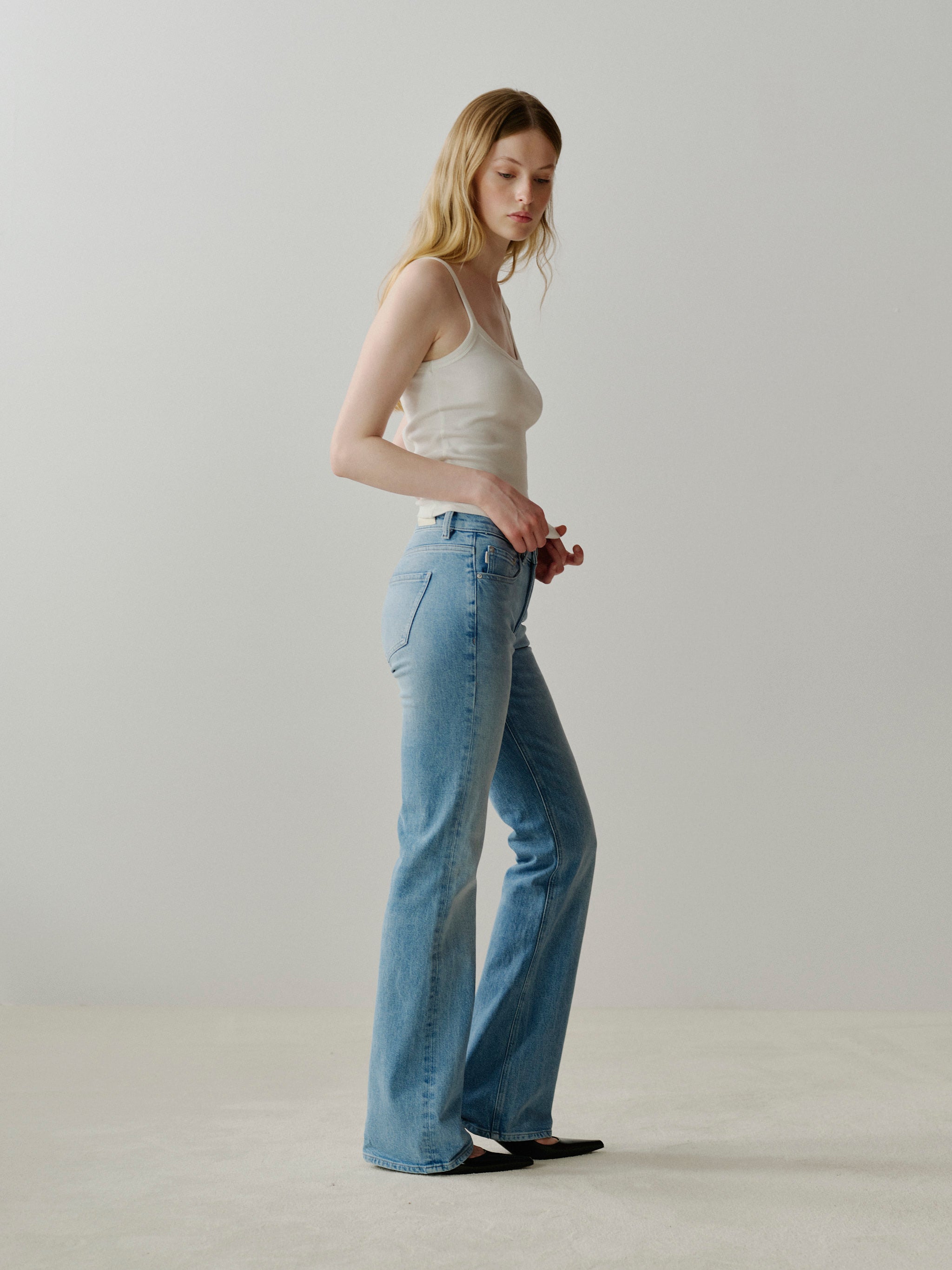 Woman wearing a white tank top and light blue jeans against a plain background