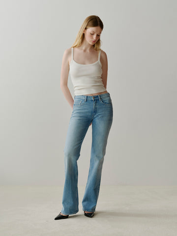 Woman wearing a white tank top and blue jeans against a plain background