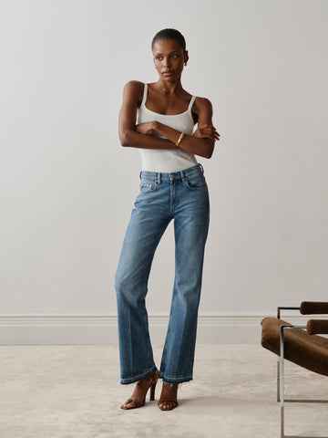 Woman wearing blue jeans and a white top standing in a minimalistic room.